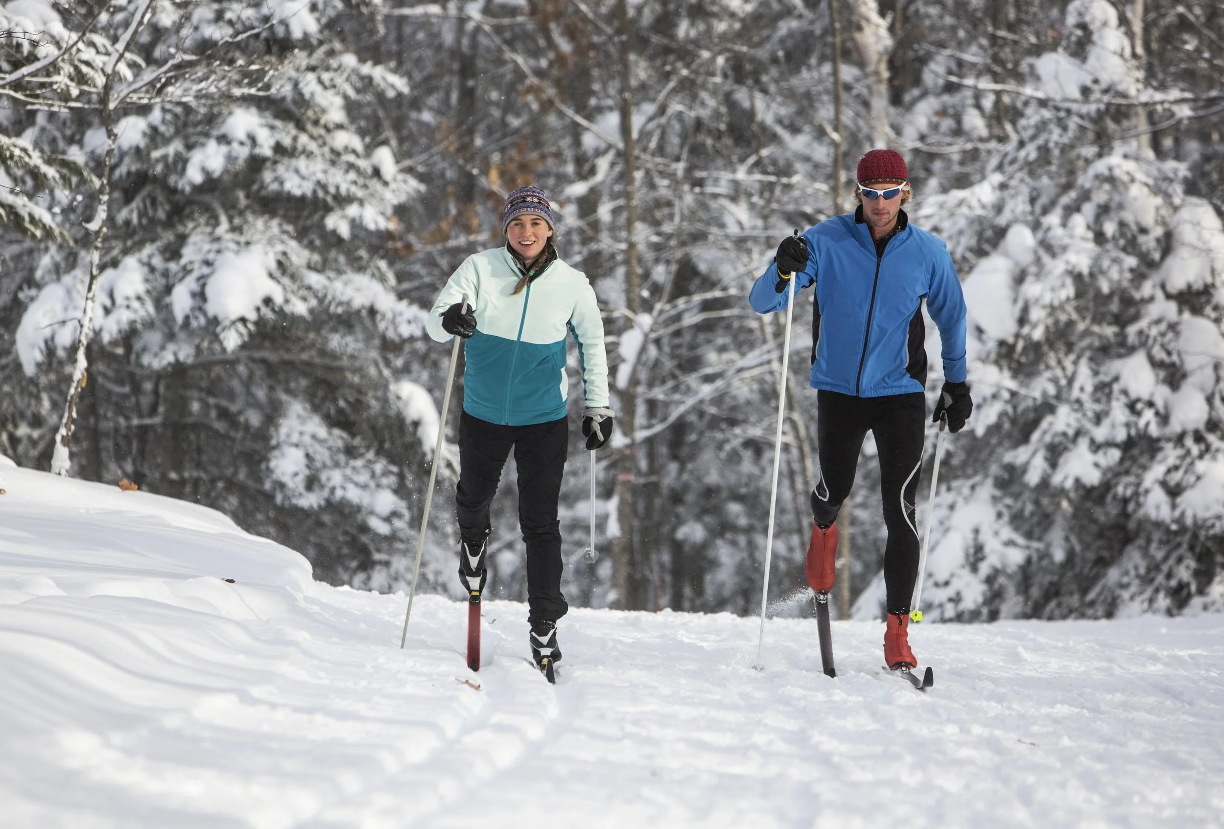 A man and woman cross-country skiing on a snowy trail through the woods at Timber Bay Lodge