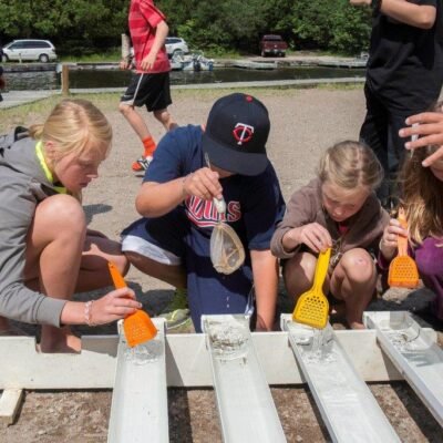 Children using plastic scoops to fill containers with water outdoors.