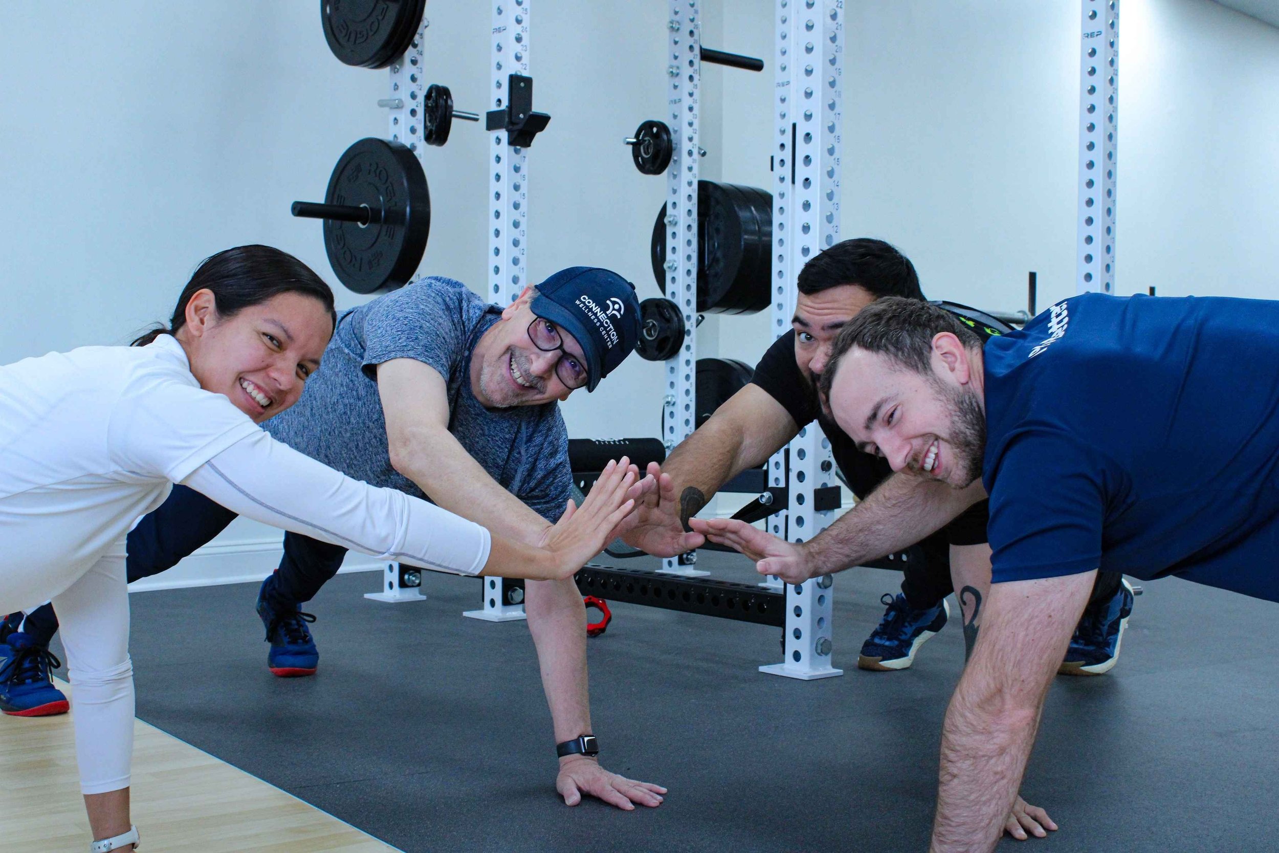 Four people in a gym doing a push-up competition, high-fiving each other.