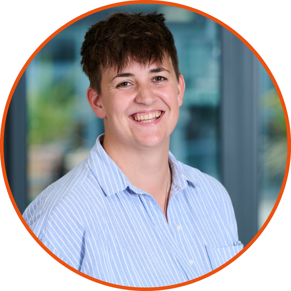 Kim Stuart-Thomas, founder of KAST Marketing. She has short brown hair and is wearing a light blue and white striped button-up shirt. She's smiling at the camera, standing indoors with a blurred window background.