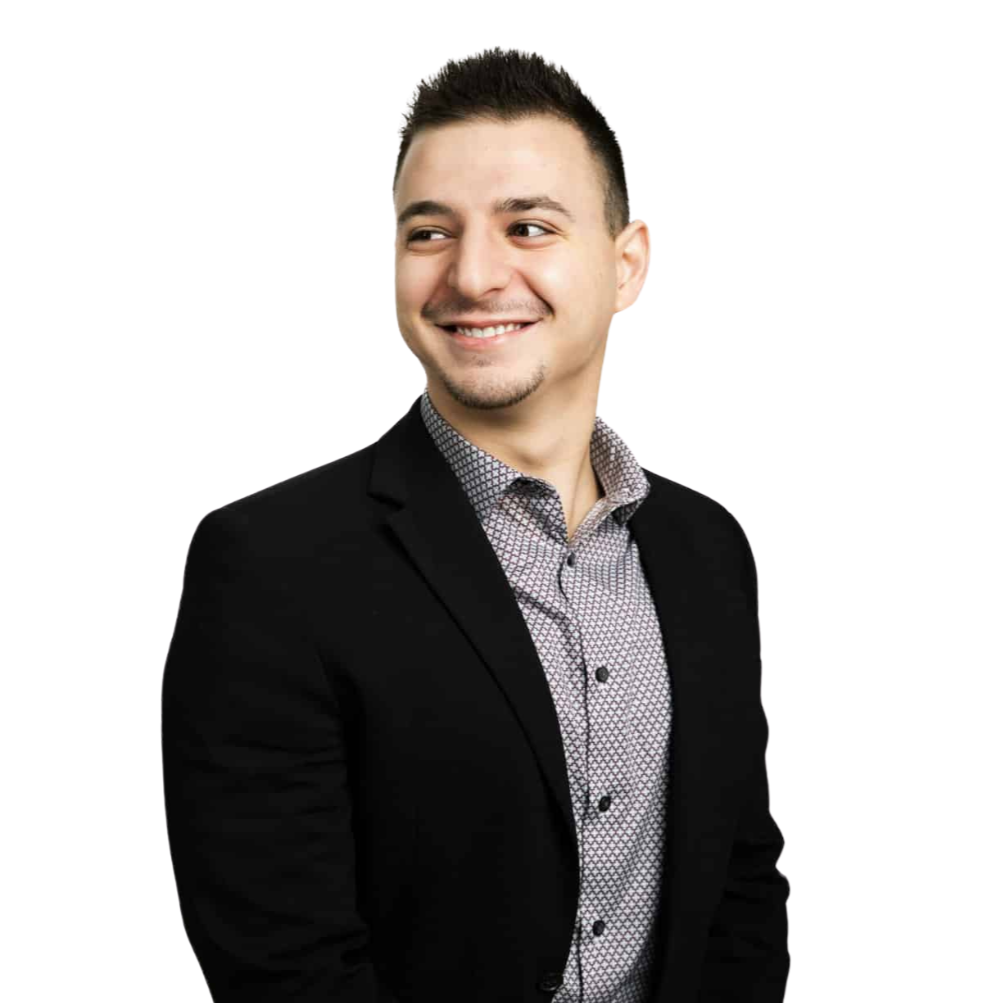 A smiling man with short dark hair wearing a black blazer and a patterned shirt, against a plain white background.