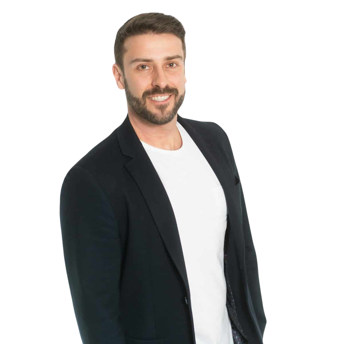 A man with brown hair and a beard, wearing a black blazer and white t-shirt, smiling against a plain white background.