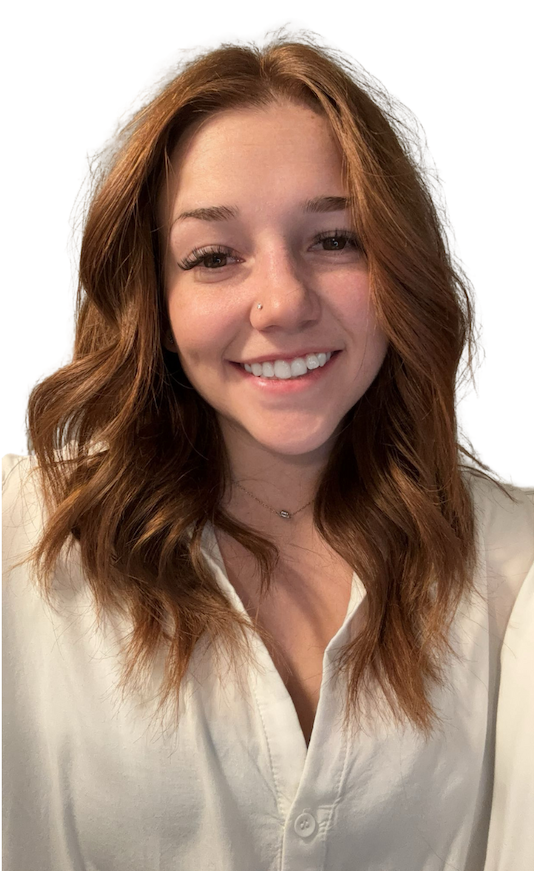Young woman with wavy red hair, smiling, wearing a white blouse, and a small nose piercing.