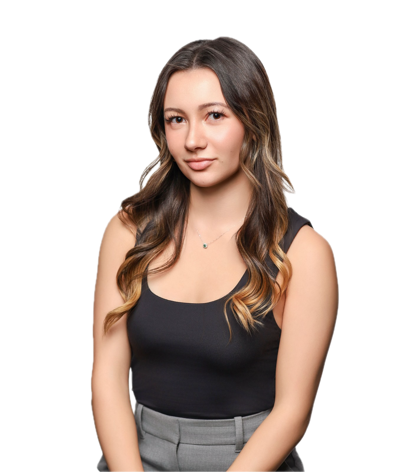 A young woman with long, wavy brown hair wearing a black sleeveless top and gray pants, looking at the camera with a slight smile, against a white background.