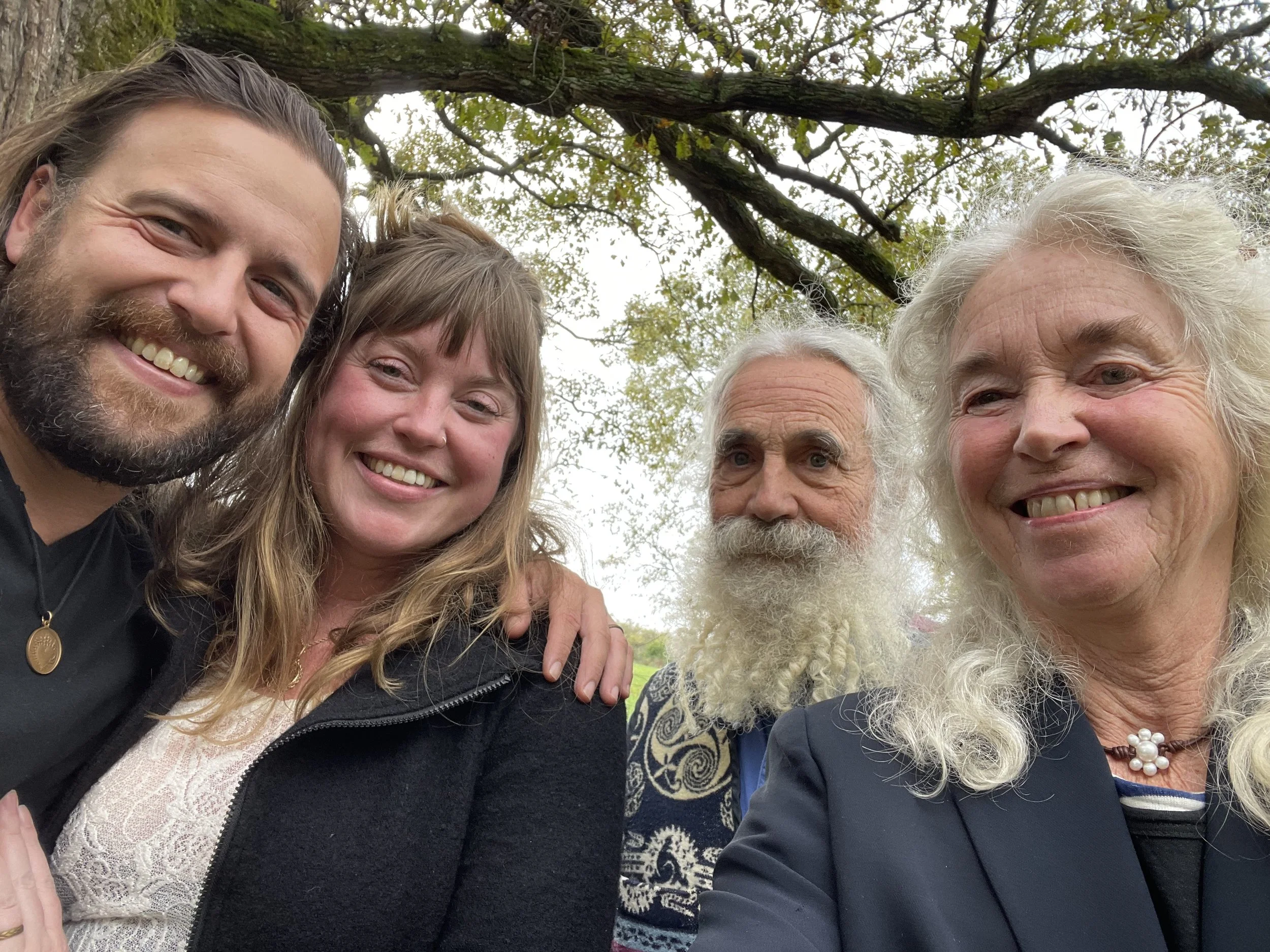 A group of five smiling people taking a selfie outdoors under a tree