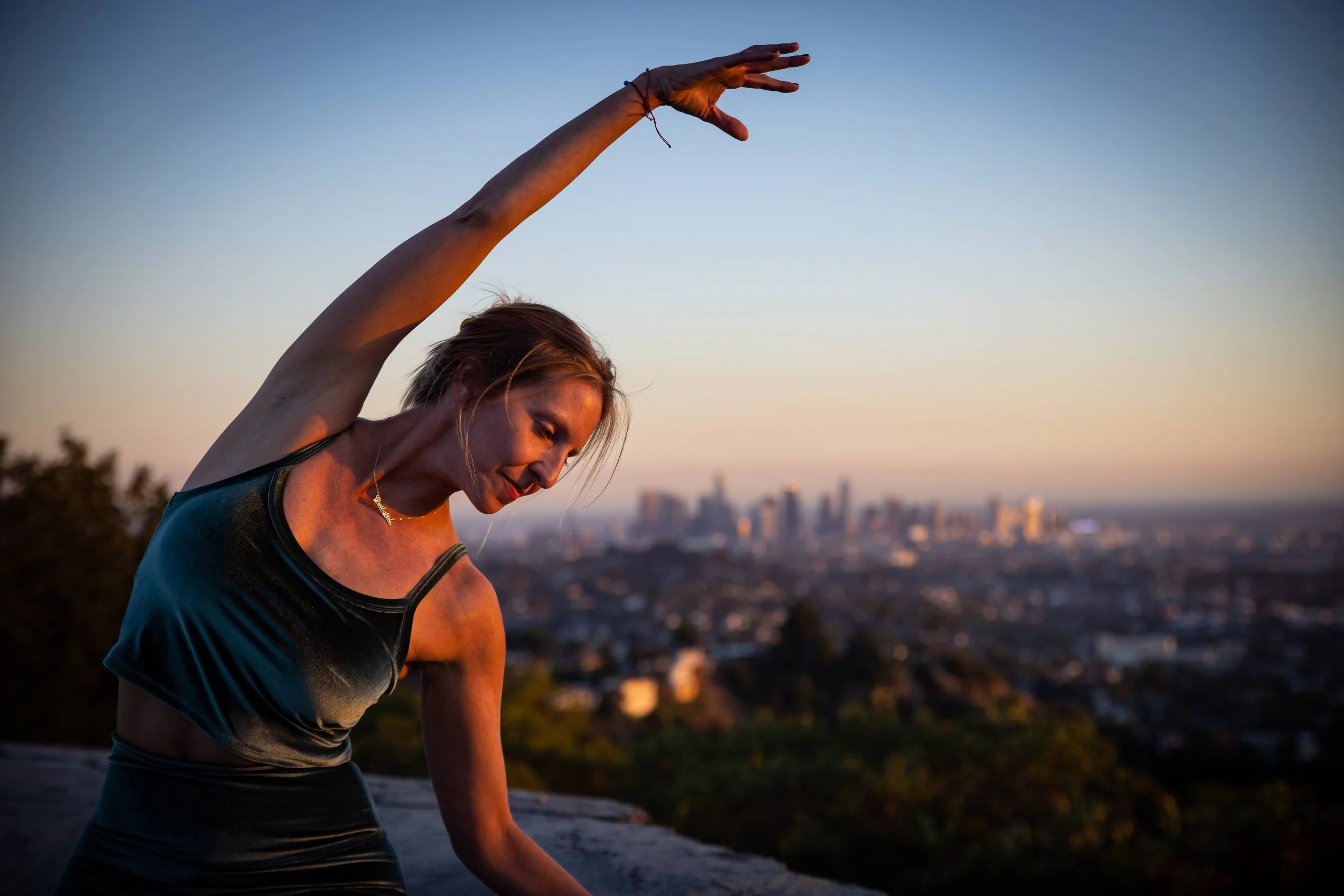 Emily Phillips, Corporate Yoga Facilitator, in a slight side bend with a city scape sunset blurred behind her