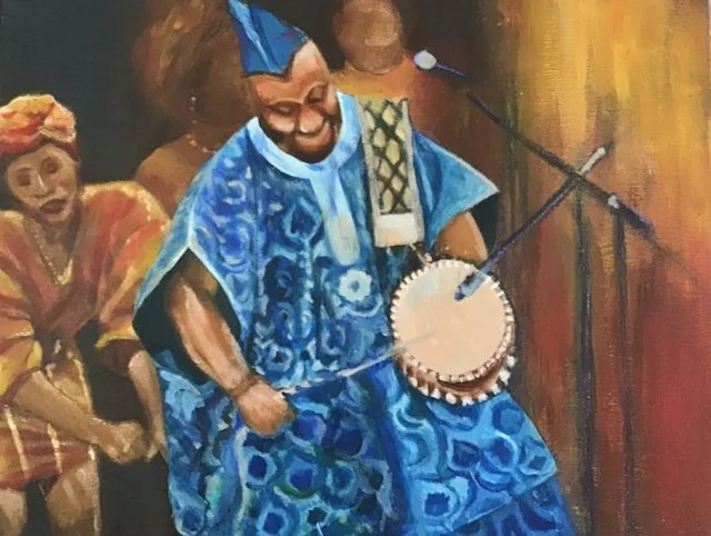 A man wearing traditional African attire and a headwrap, playing a drum with a drumstick at a cultural event.