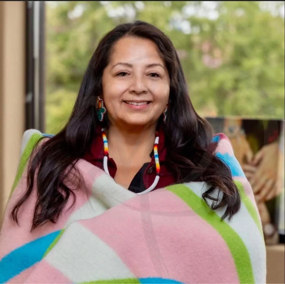 Portrait of a woman with black hair wearing a black blazer and white shirt against a white background.