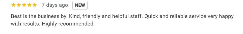 Modern building with wood and metal exterior, large glass window, set against mountains with grassy terrain and small trees in the foreground.