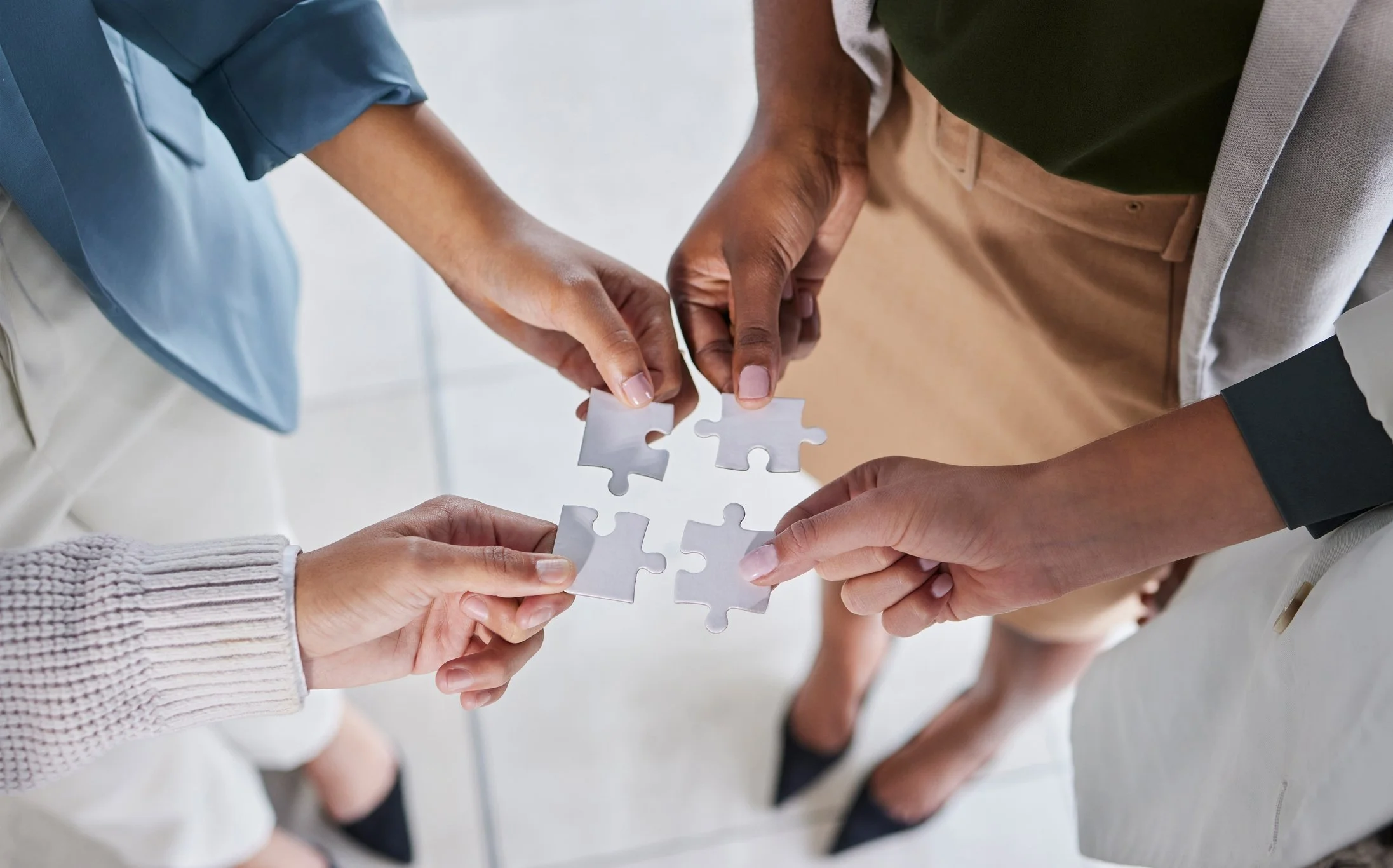 Four people coming together to assemble four interlocking puzzle pieces.
