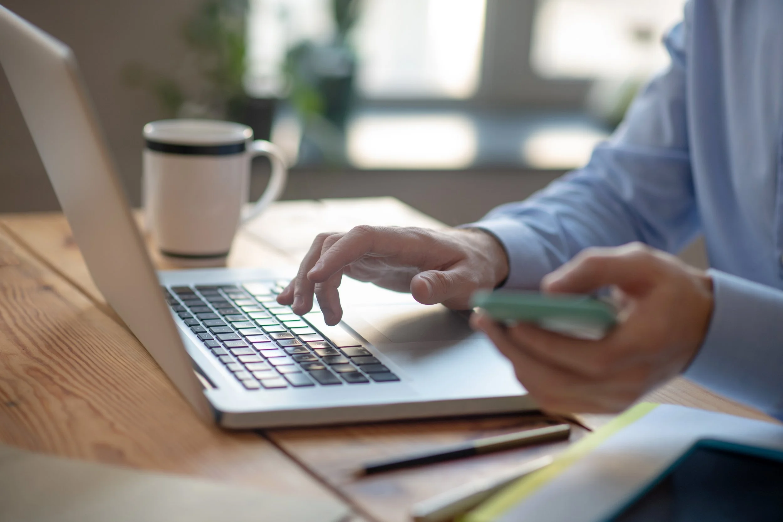 Person working on a laptop at a wooden desk with a coffee mug in the background.
