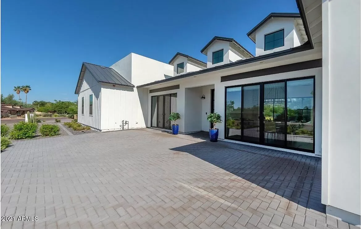 The front elevation of this 2019-built home showcases a stunning modern design defined by expansive floor-to-ceiling glass that fills the interior with natural light while framing beautiful views of the landscaped front yard. A spacious paver patio e