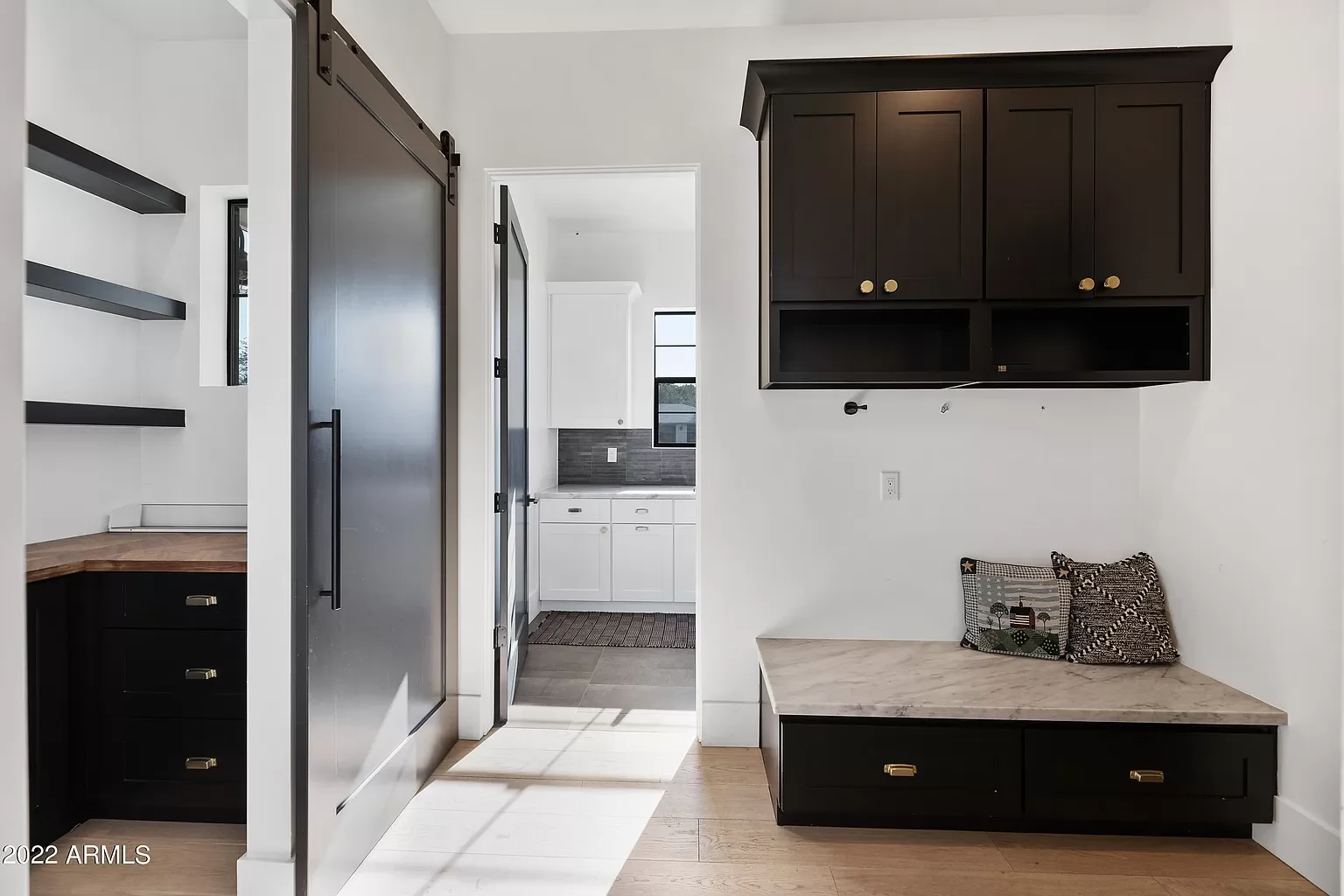 Kitchen with black cabinets, built-in shelves, and a marble bench with pillows.