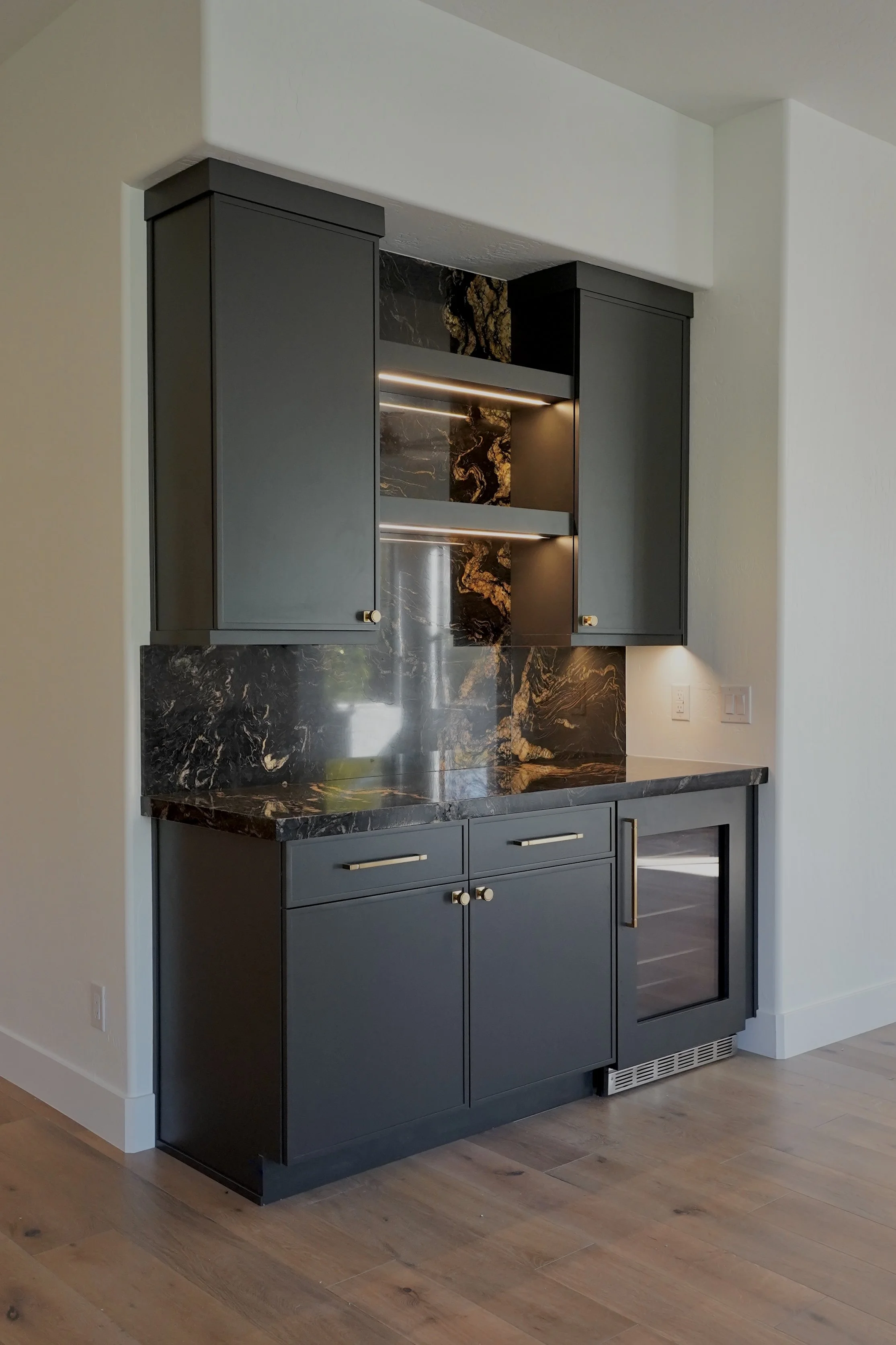 Kitchen area with dark cabinetry, black marble backsplash, and a built-in mini fridge with a glass door.