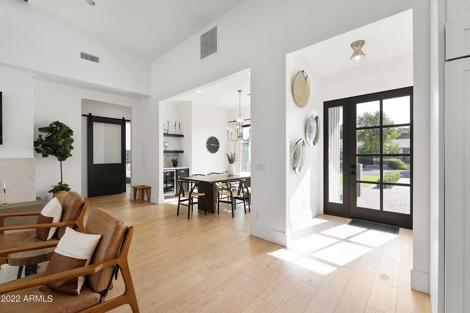 Modern minimalist interior living space with a view of the dining area, entry door, and natural light streaming through windows and door