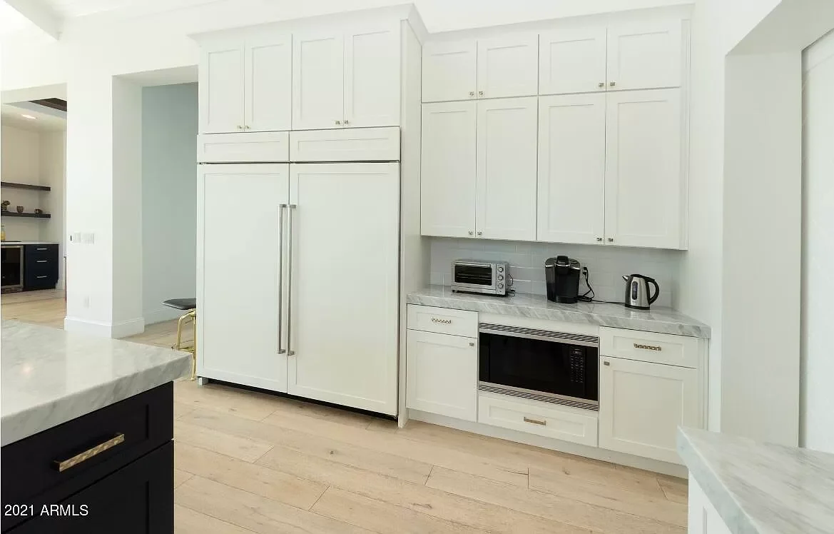 Kitchen with white cabinets, a built-in microwave, and black appliances, including a refrigerator, coffee maker, and toaster, with marble countertops and light wooden flooring.