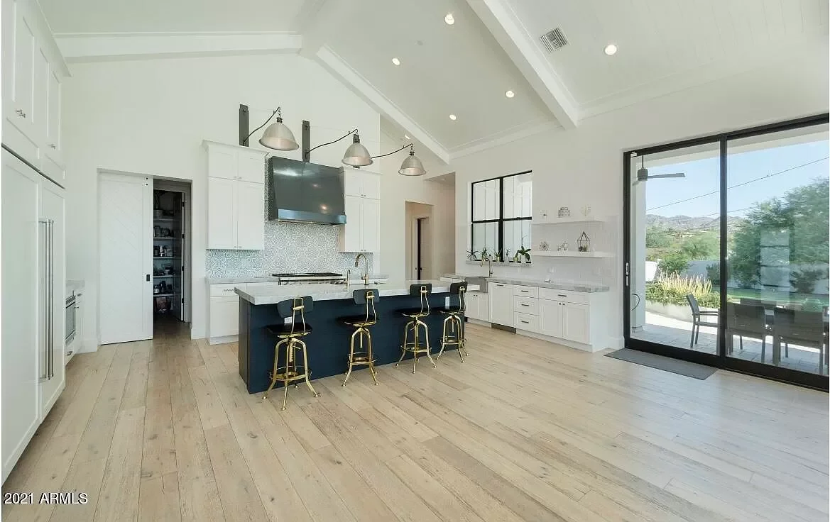 Modern kitchen with white cabinets, black island with gold stools, large sliding glass door, and outdoor patio.