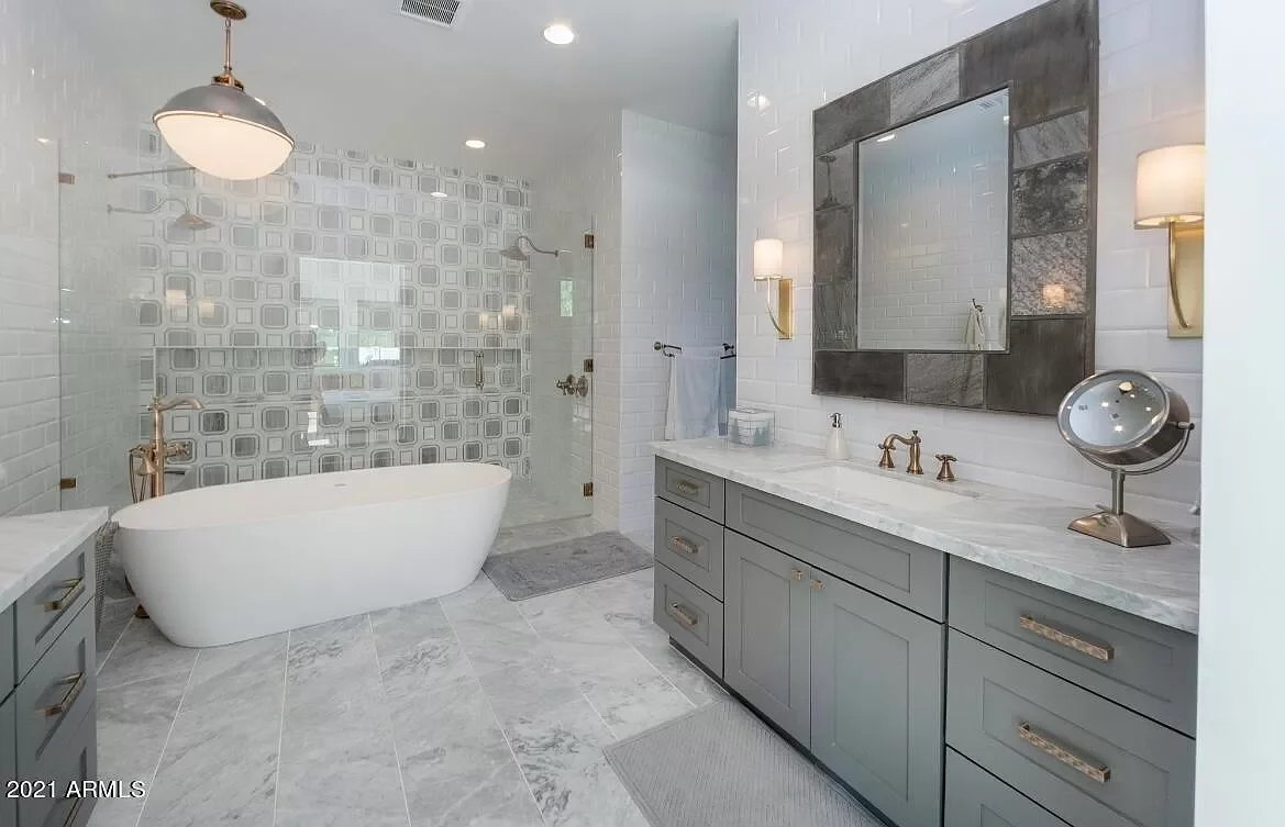 Modern bathroom with a freestanding bathtub, gray cabinetry, marble countertops, and a large framed mirror.