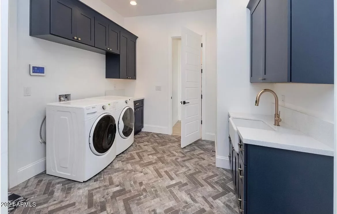 Laundry room with front-loading washer and dryer, blue cabinets, white countertops, a white door, and wood-look tile flooring.