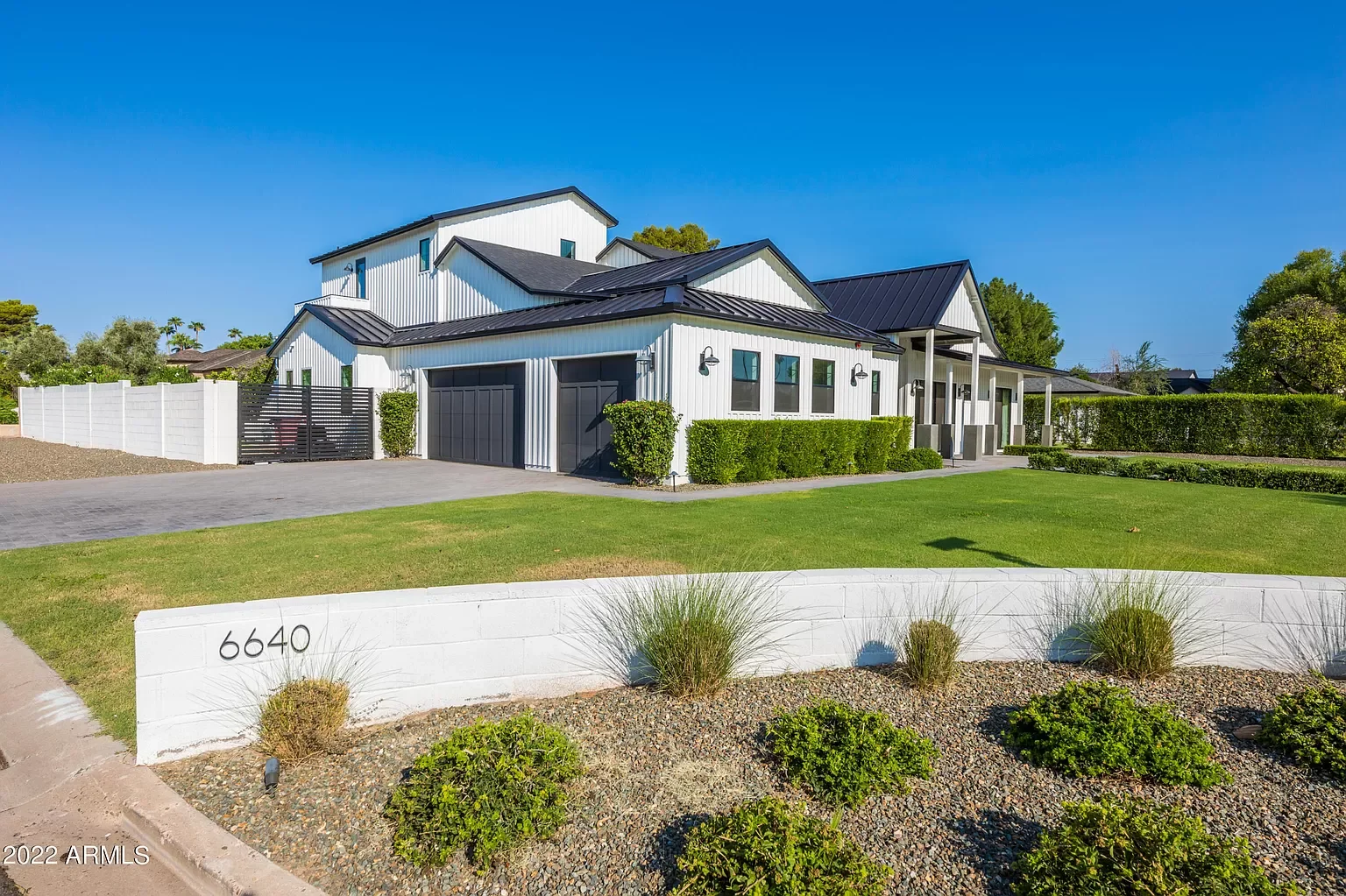 Modern white house with black roof, green shrubs, and a well-manicured lawn.