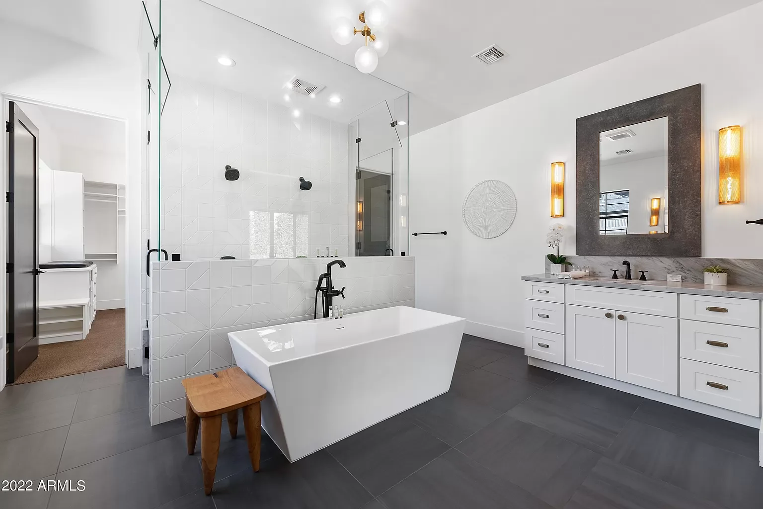 Modern bathroom with freestanding bathtub, white vanity with large mirror, framed with dark gray, decorated with wall sconces, and a walk-in shower with glass enclosure and black fixtures.