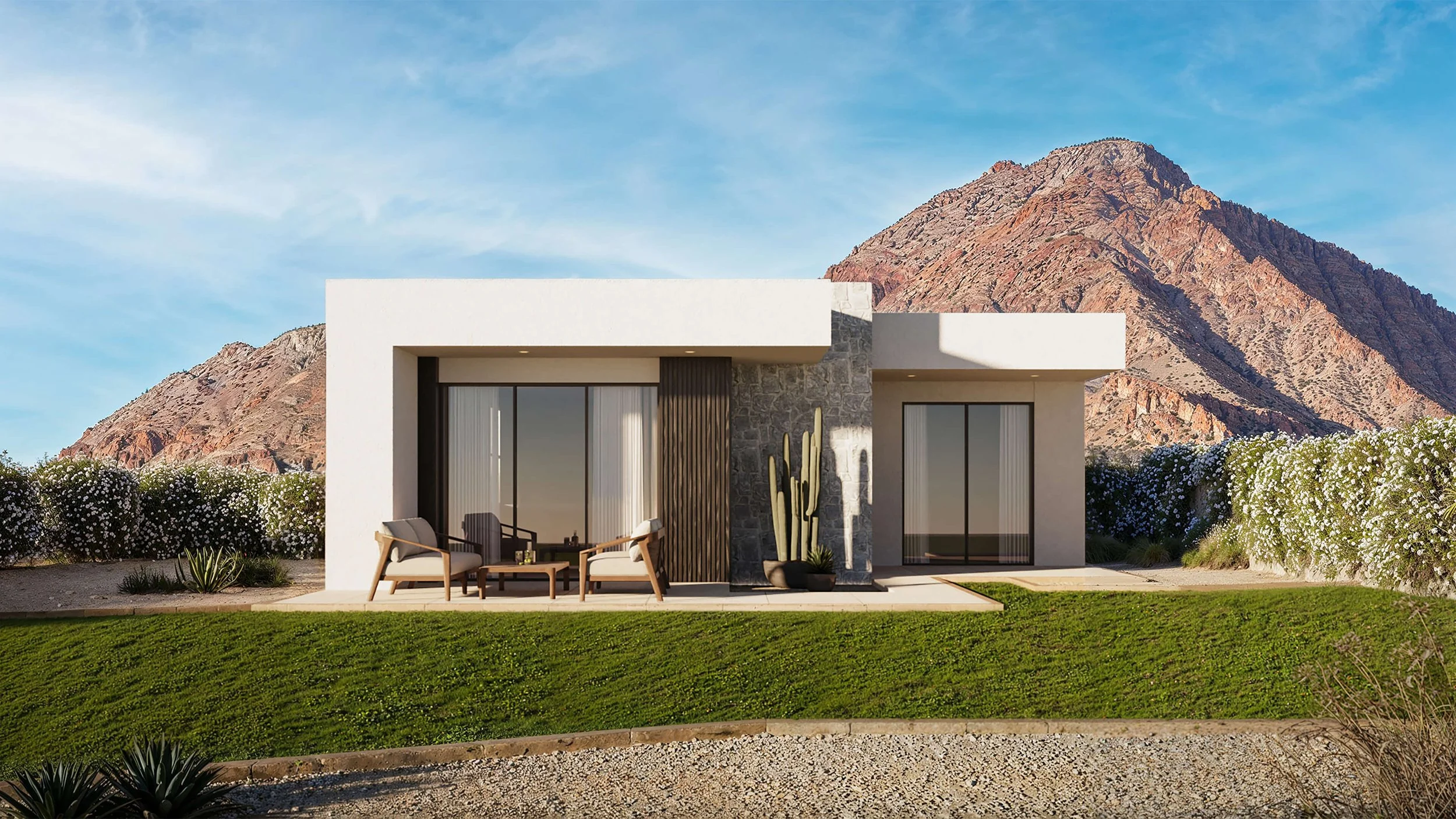 Modern house with white exterior, large sliding glass doors, and stone accents, surrounded by desert landscaping, with a mountain in the background and a seating area with chairs and a table in the front yard.