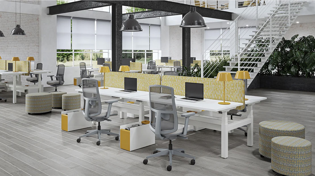 Modern open-plan office with white desks, gray ergonomic chairs, yellow lamps, patterned ottomans, and large windows with blinds
