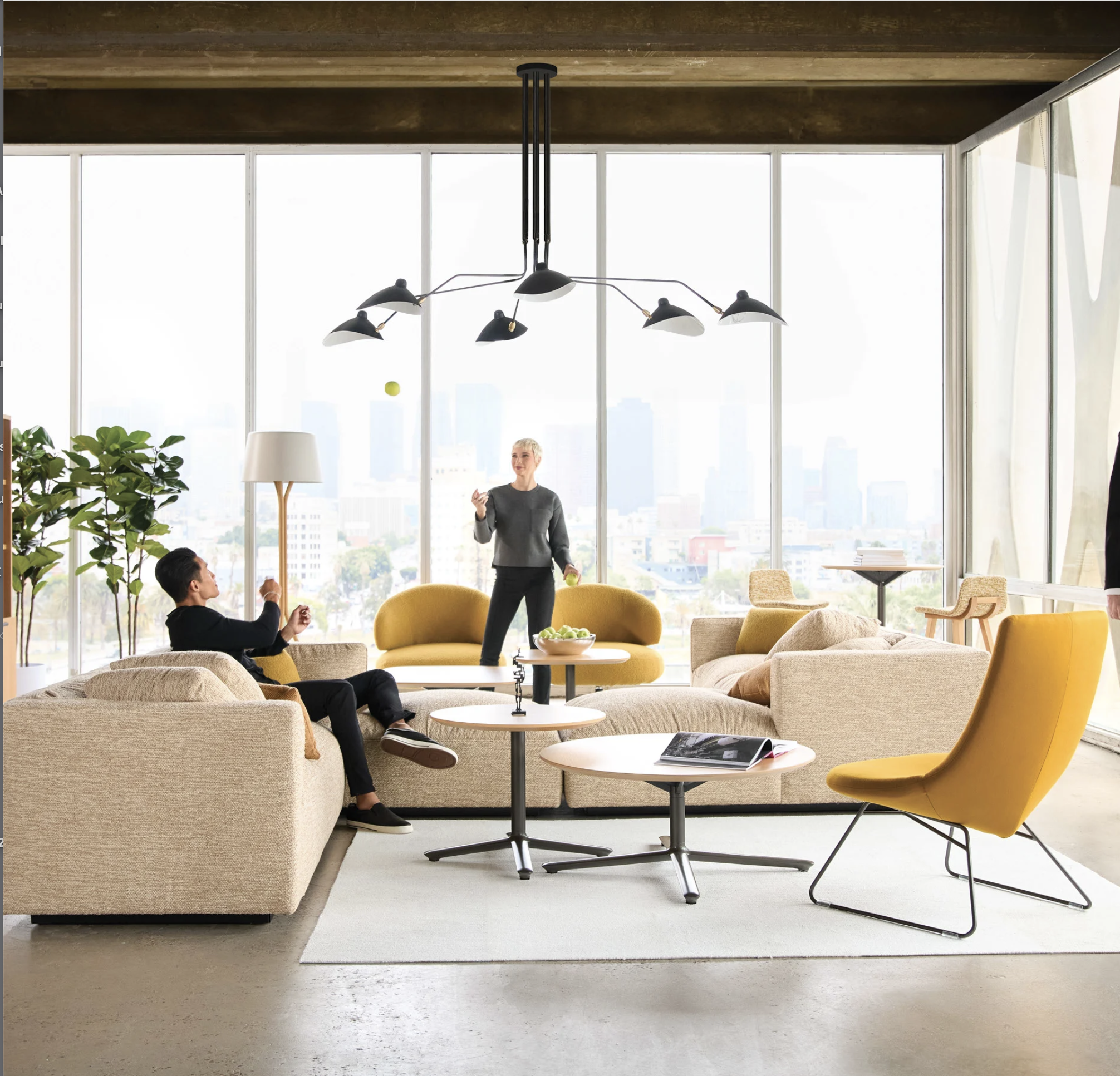 People in a modern lounge with large windows, sofa, yellow armchair, coffee tables, potted plant, and a person juggling tennis balls.