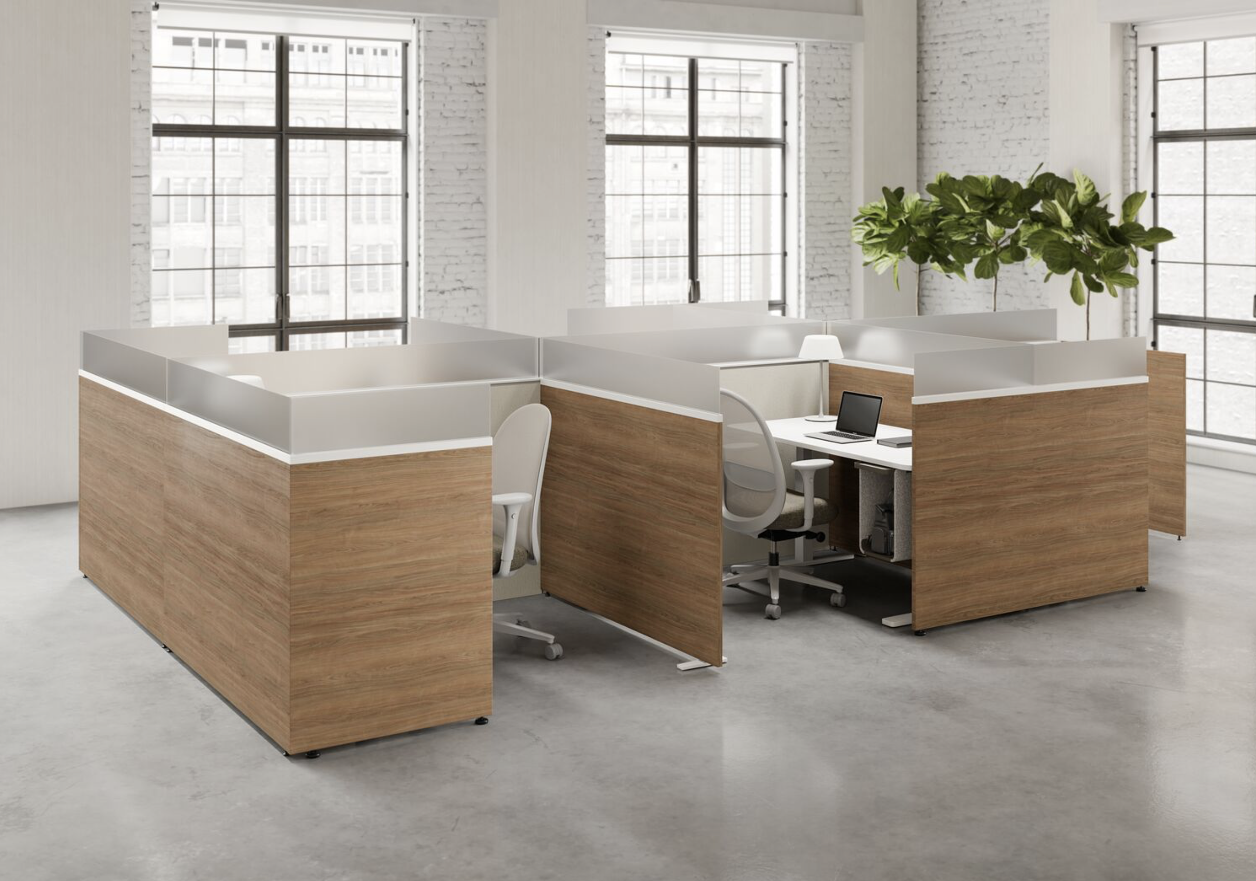 An office space with four workstations arranged in a square, each with a white desk, white ergonomic chair, and partition panels. There is a laptop, a desk lamp, and a notebook on one of the desks. The room has large windows, white brick walls, and a