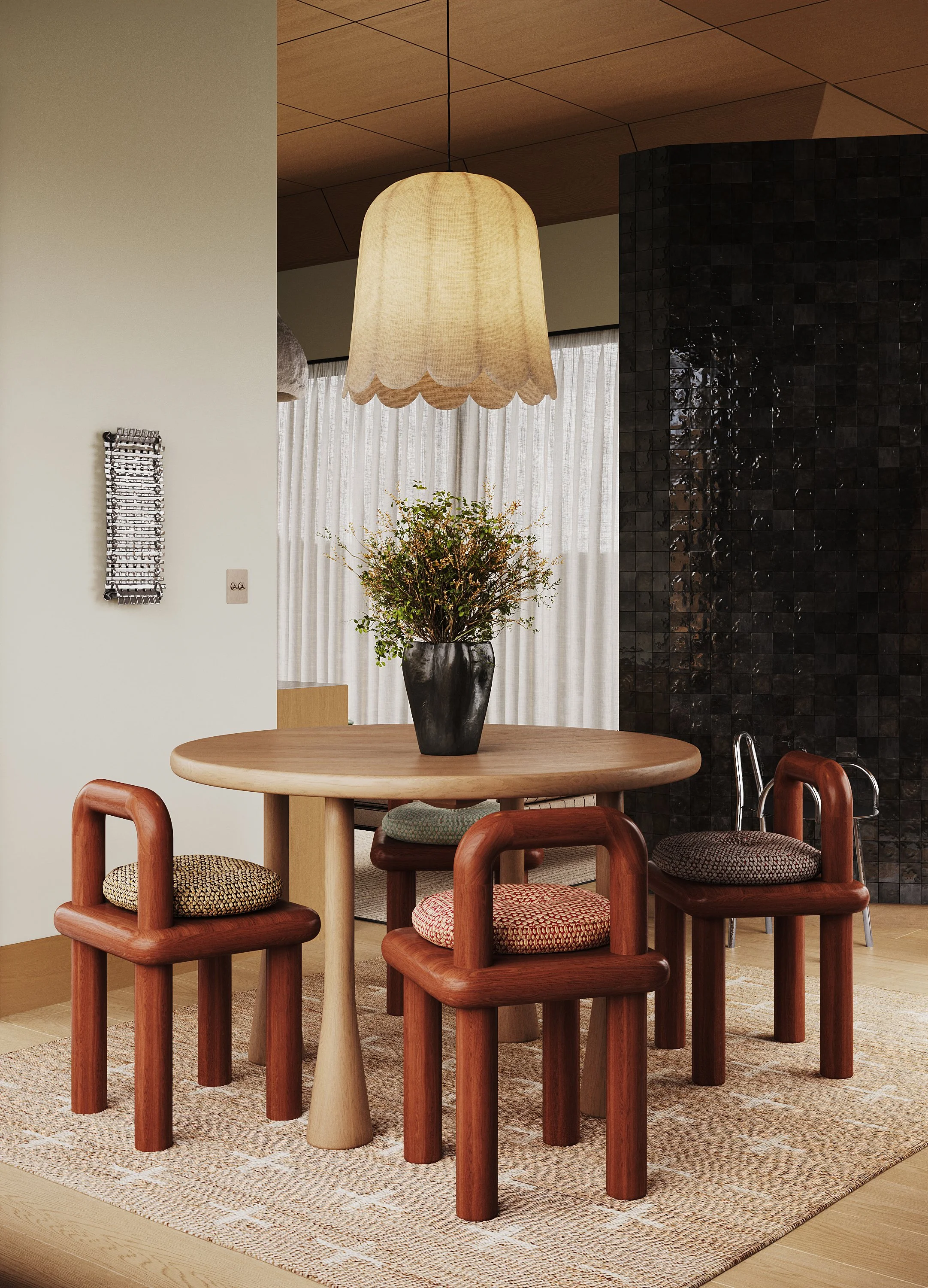 A cozy dining room with a round wooden table surrounded by four wooden chairs with patterned cushions. A black vase with greenery sits in the center of the table. A beige lamp hangs above, and a dark tiled wall is visible in the background.