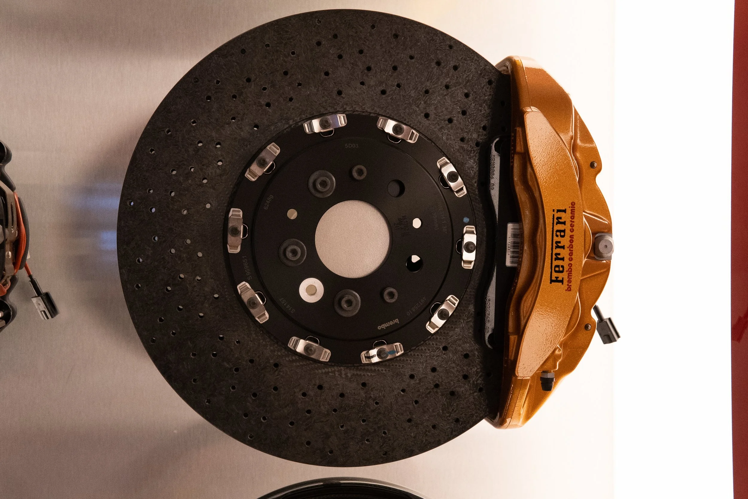 A carbon-ceramic yellow brake caliper with 'Ferrari' branding holding a large cross-drilled brake disc.