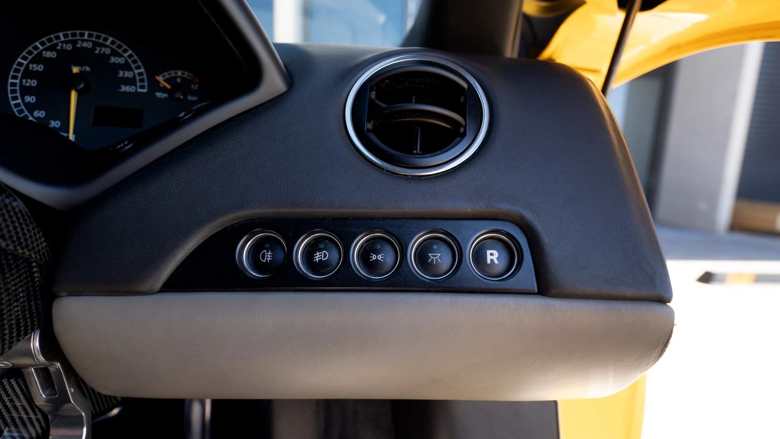 Dashboard of a yellow vehicle showing gauges and control buttons, with a circular air vent.