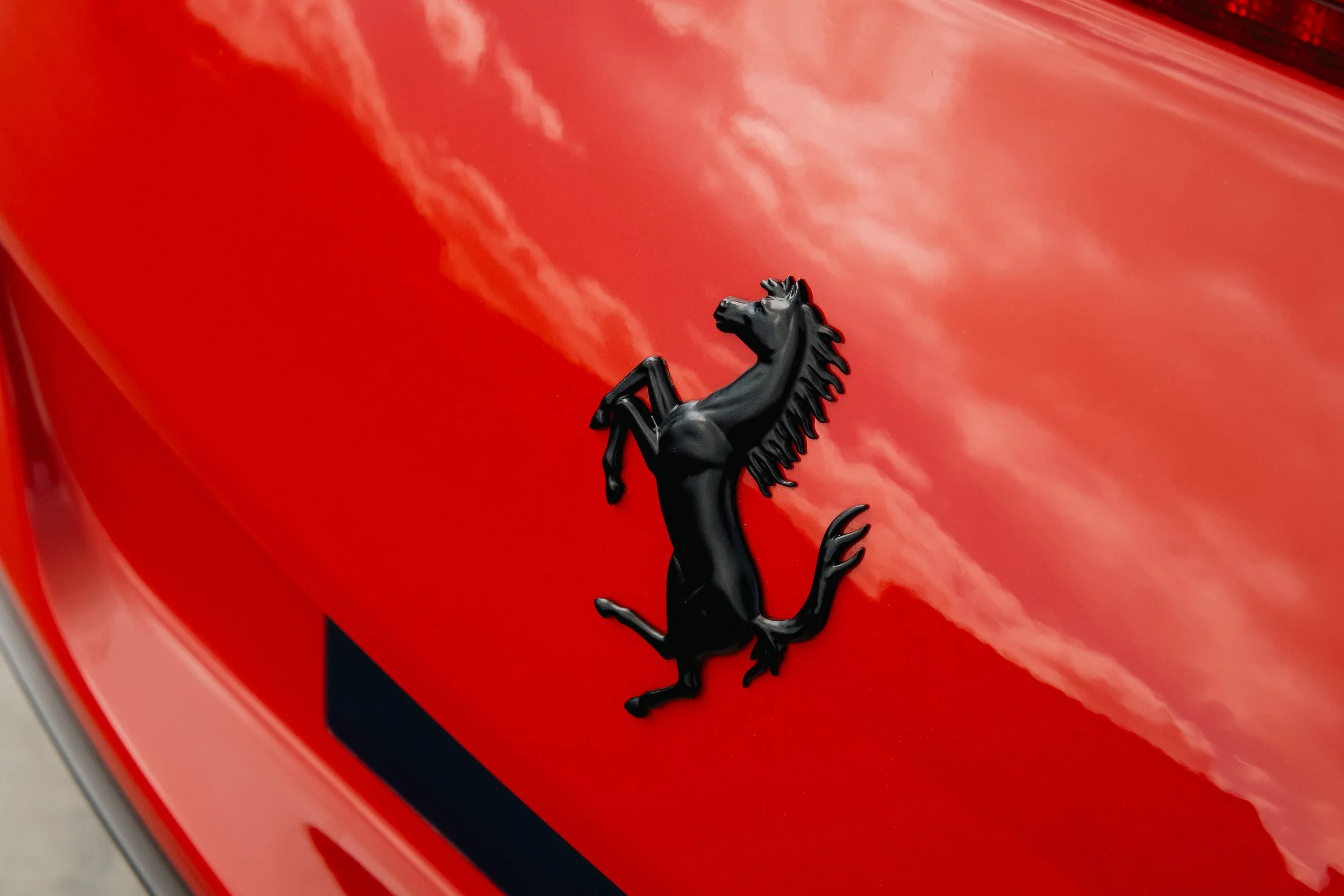 Close-up of a black prancing horse emblem on the red hood of a Ferrari sports car with reflections of the sky.