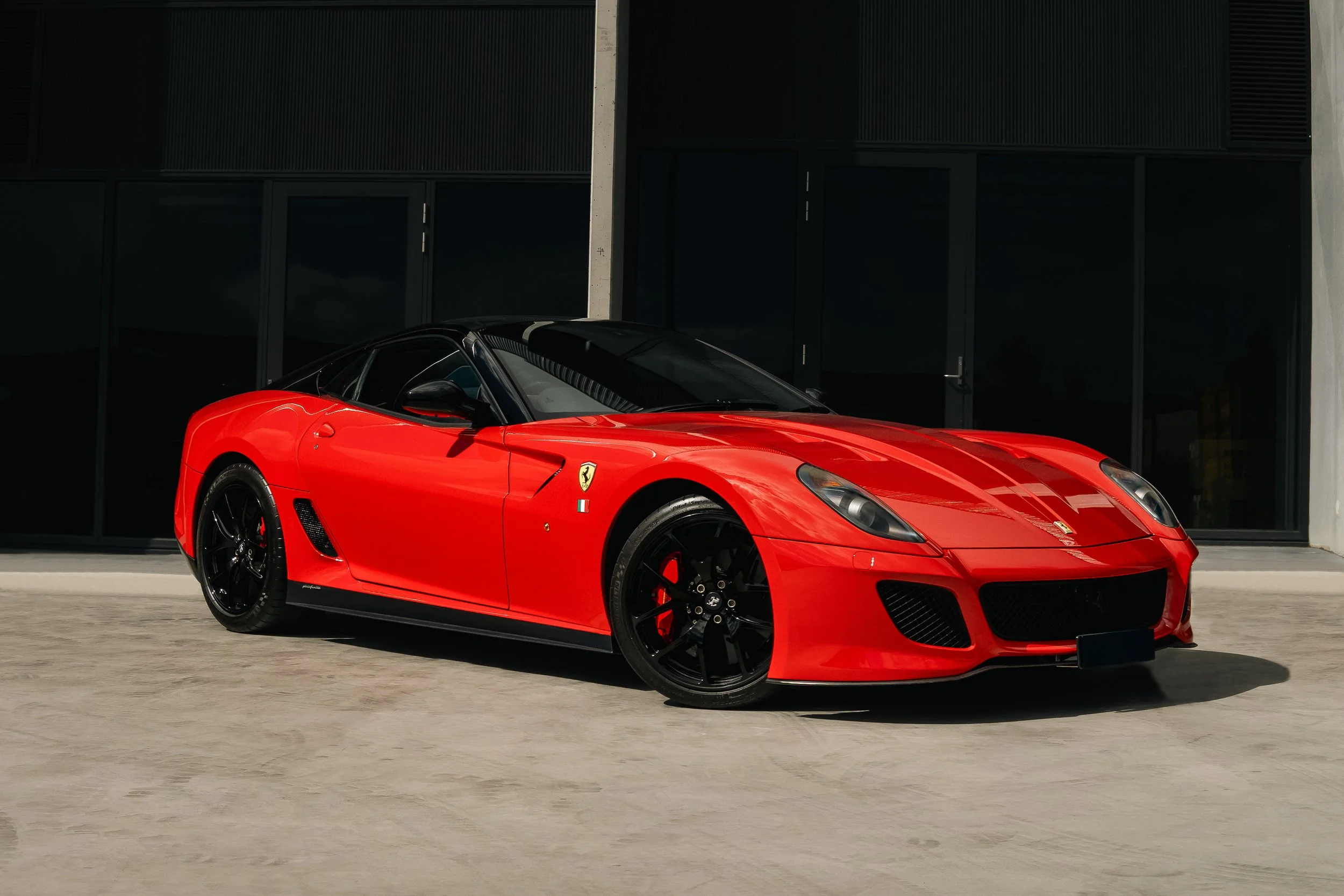 Red Ferrari 599 GTO sports car parked outside a modern building.