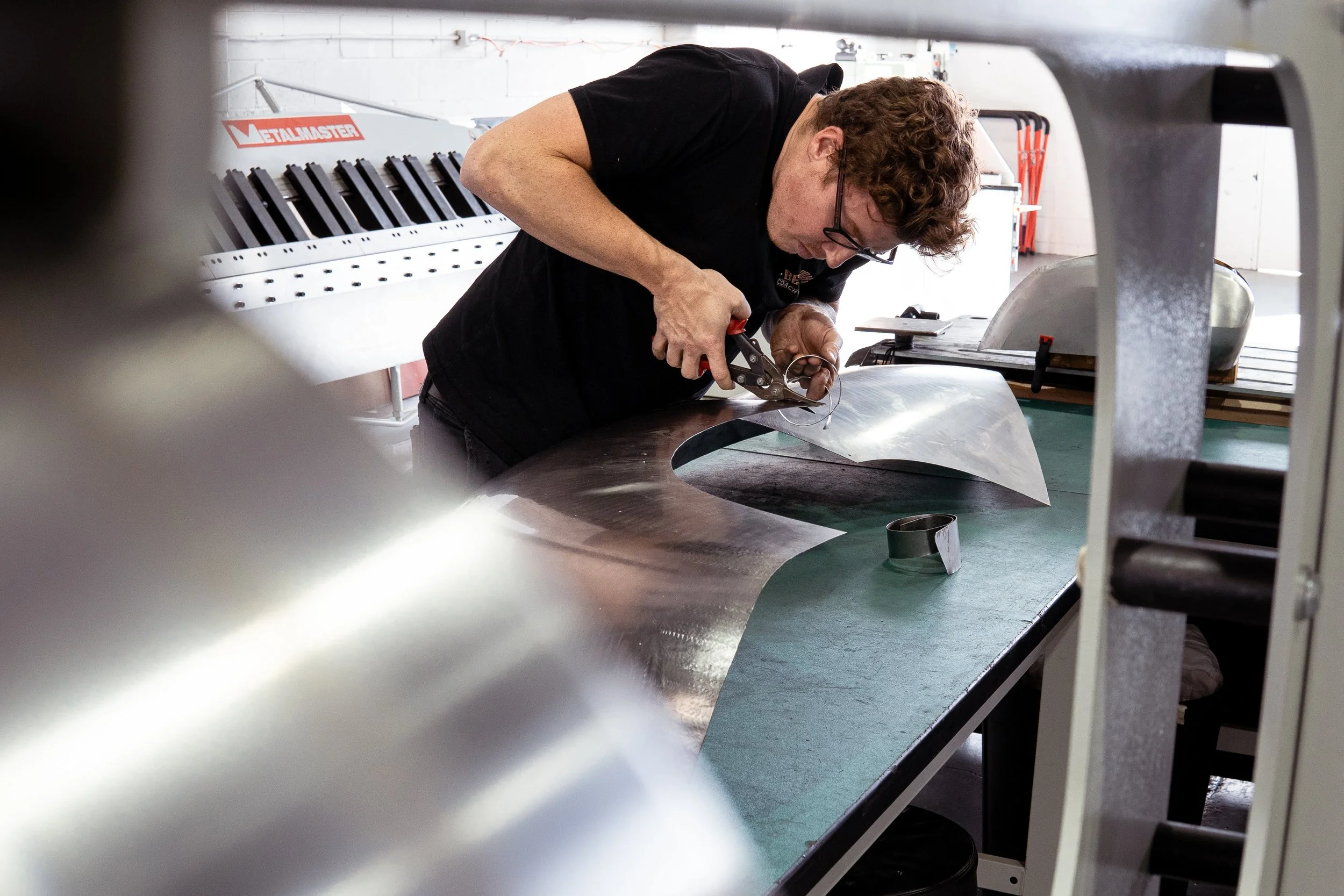 A craftsman working on a large metal sheet with a pair of pliers in a workshop.