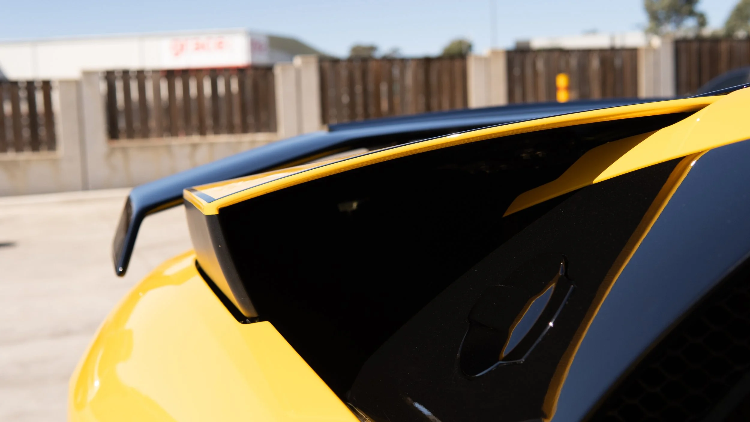 Close-up of the rear spoiler of a yellow sports car parked outdoors.