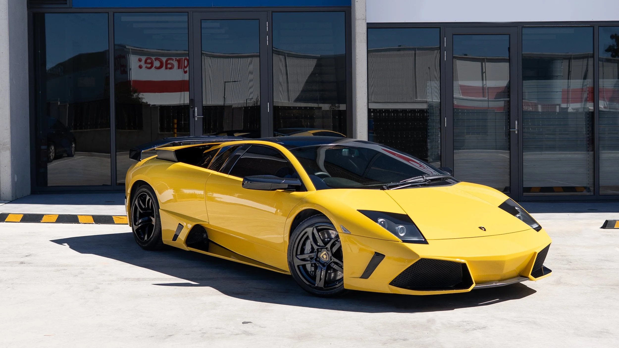 Yellow Lamborghini sports car parked in front of a modern glass building.