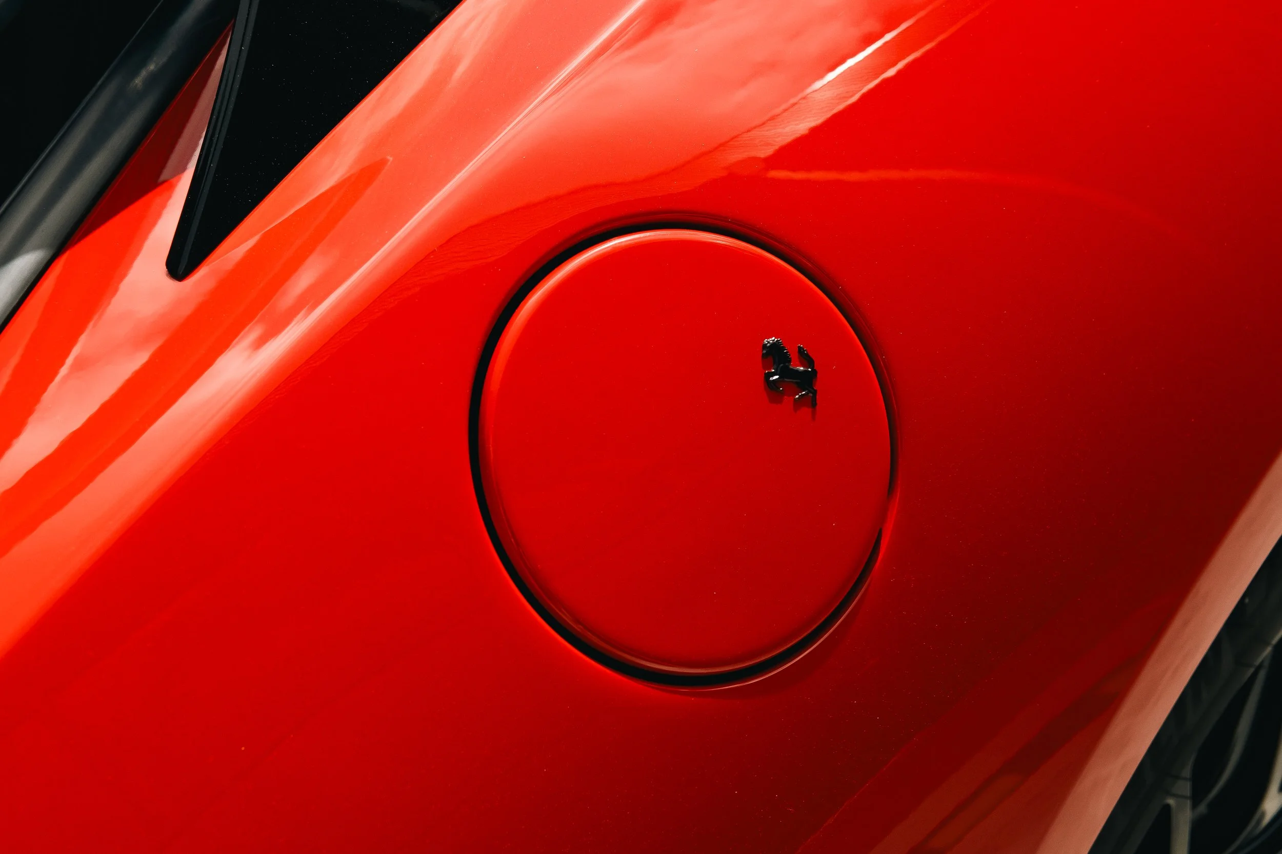Close-up of a red Ferrari car's fuel cap on the hood.