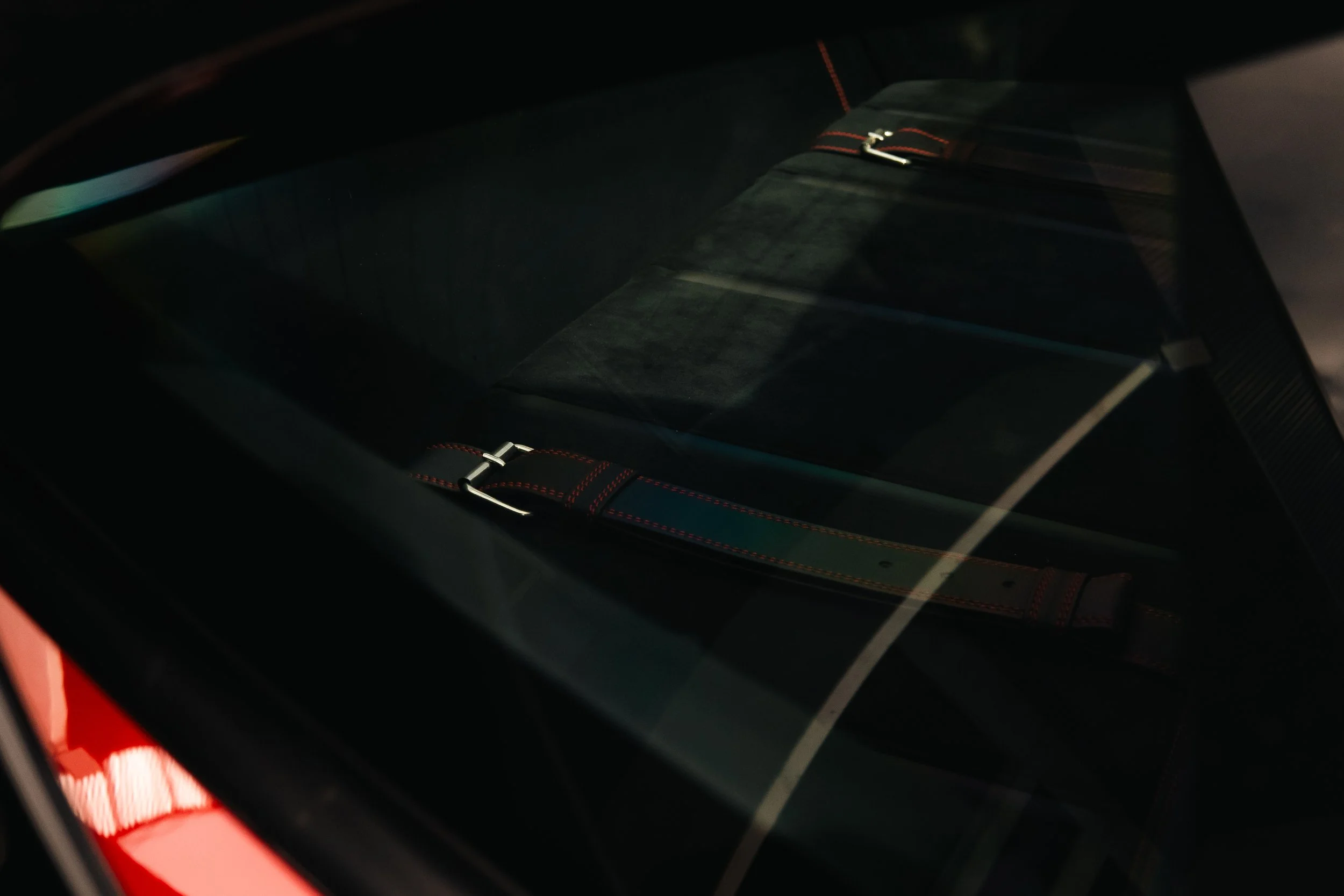 Rear view of a black car showing the back seat through the rear window, with headrest and seatbelt visible.