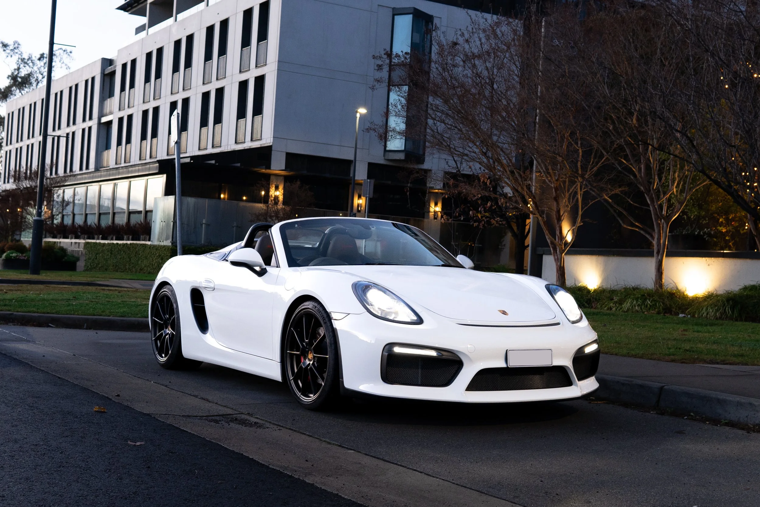 A white Porsche sports car parked on the side of a city street at dusk.