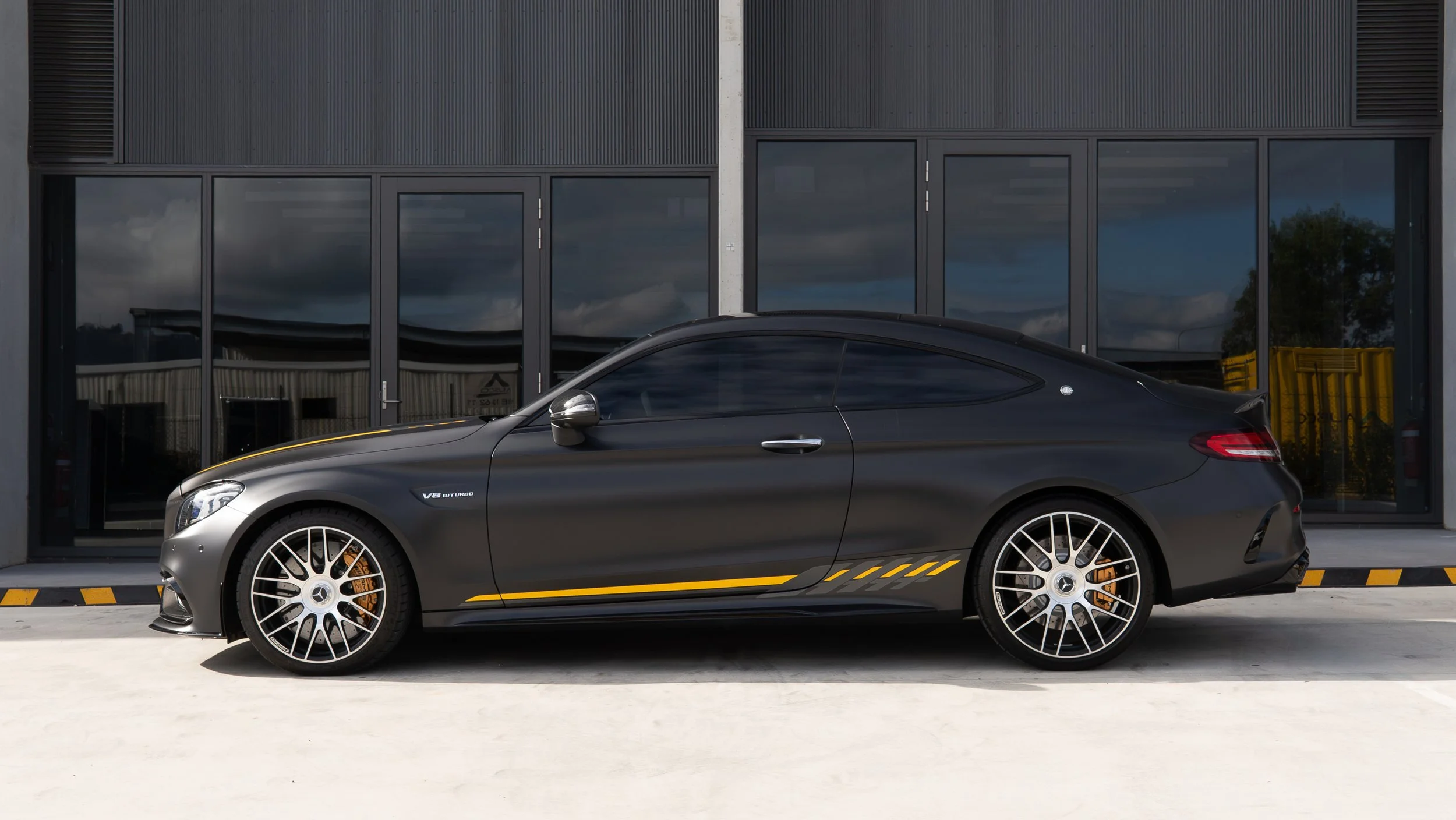 Black Mercedes C63s AMG final edition with yellow accents parked outside a modern building with glass doors
