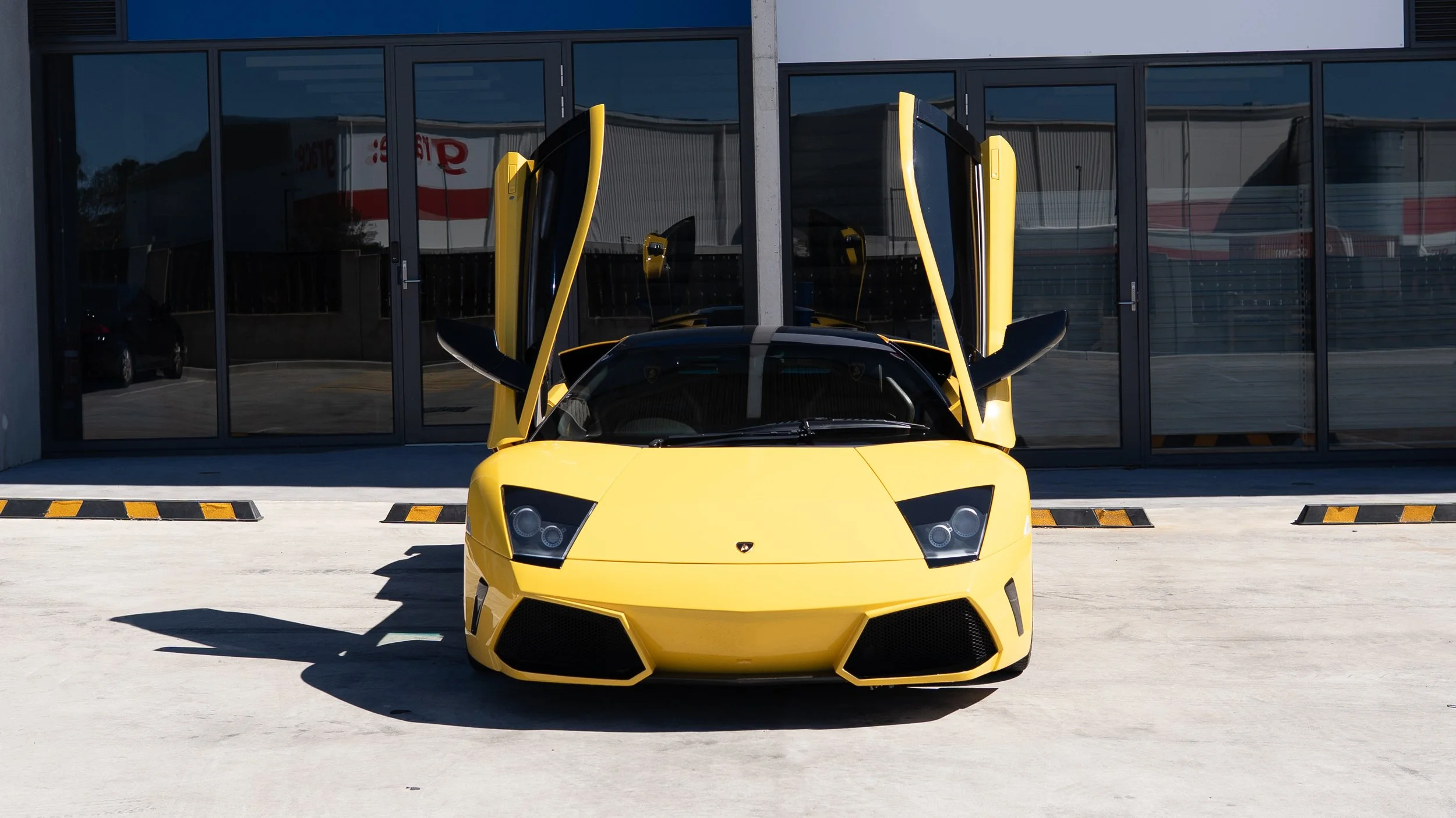 Yellow Lamborghini sports car with upward-opening doors parked outside a building with glass windows.
