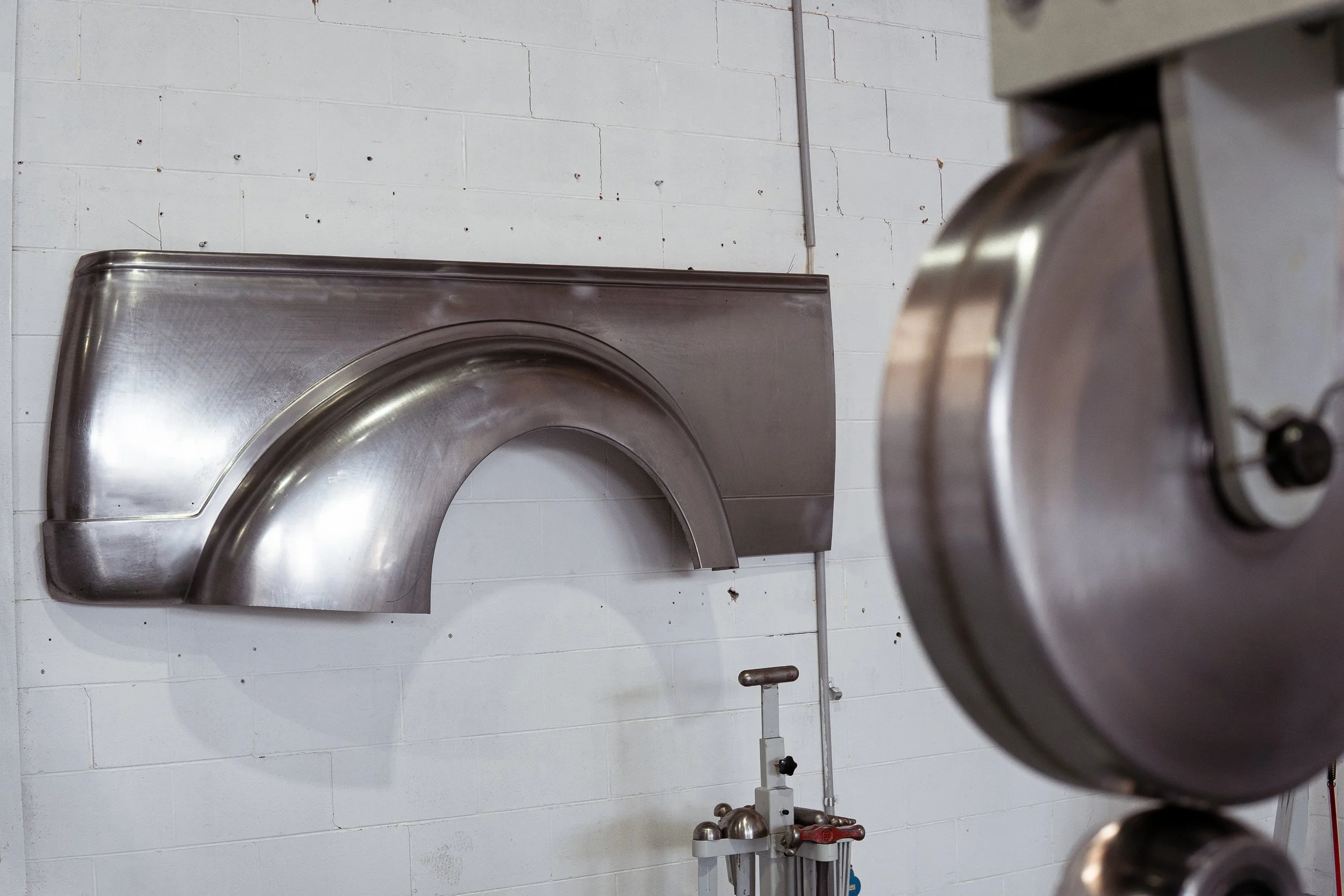 An industrial kitchen wall with a large stainless steel exhaust hood and a close-up of a metal equipment part in the foreground.