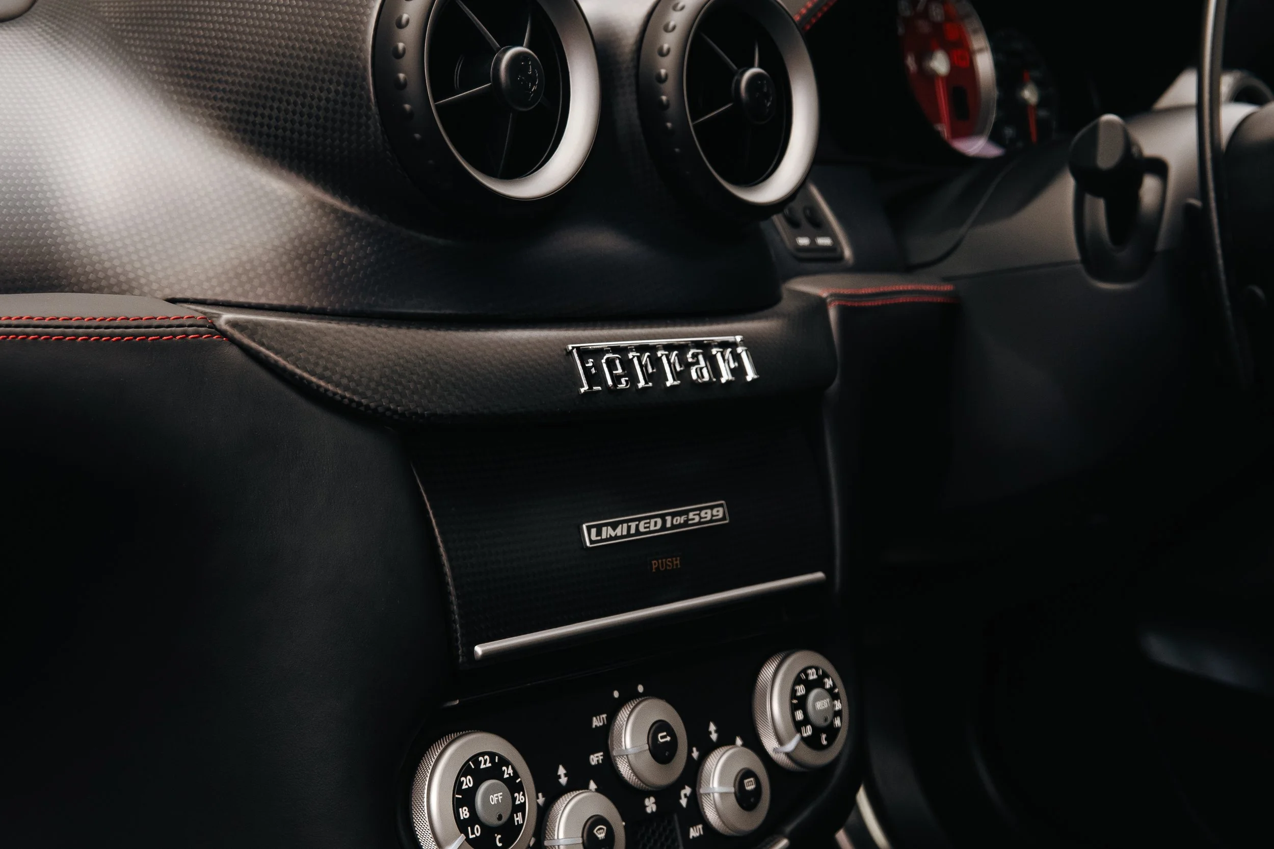 Close-up of the interior dashboard of a Ferrari, including air vents, the Ferrari emblem, and climate control dials.