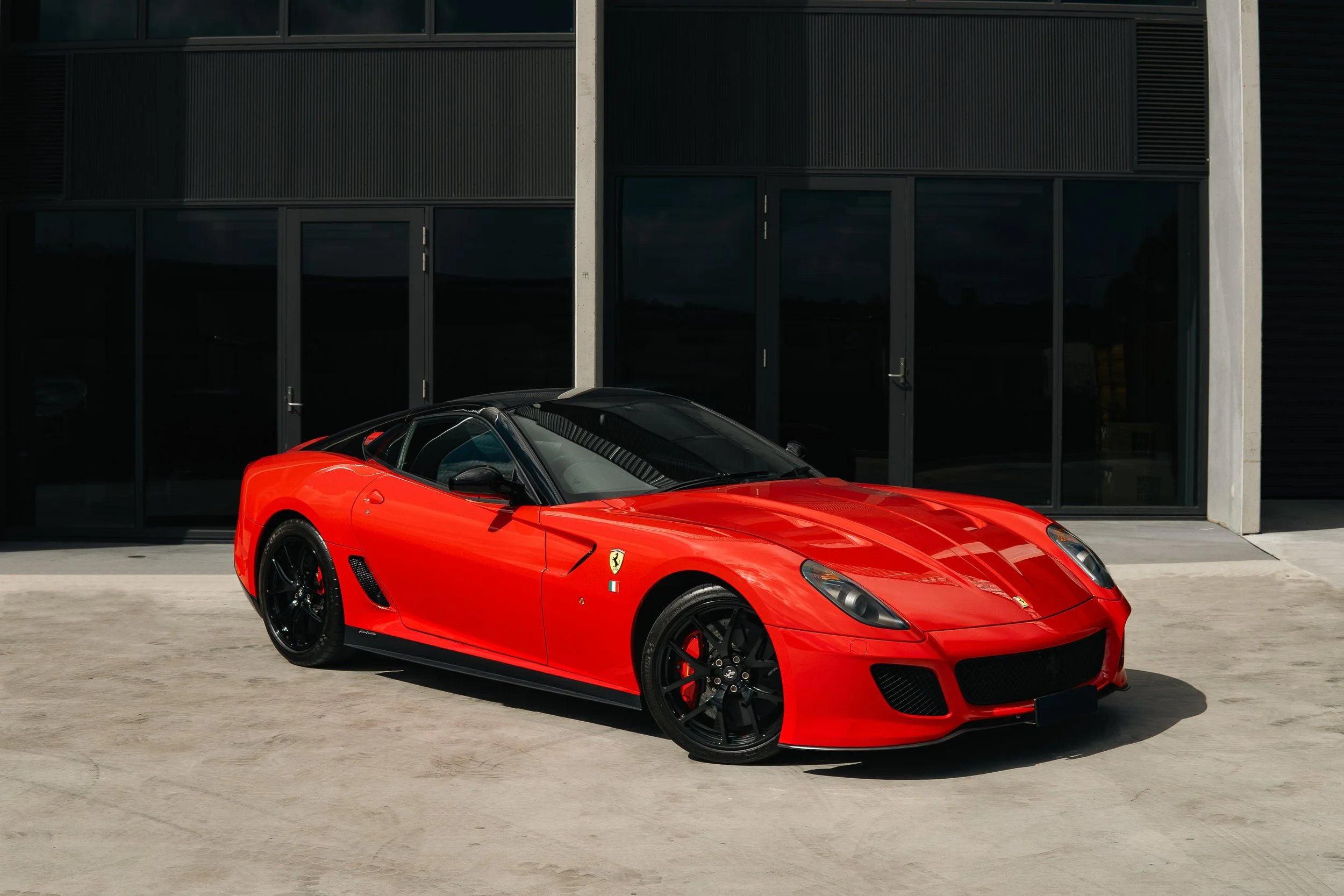 Red Ferrari sports car parked in front of a black modern building.