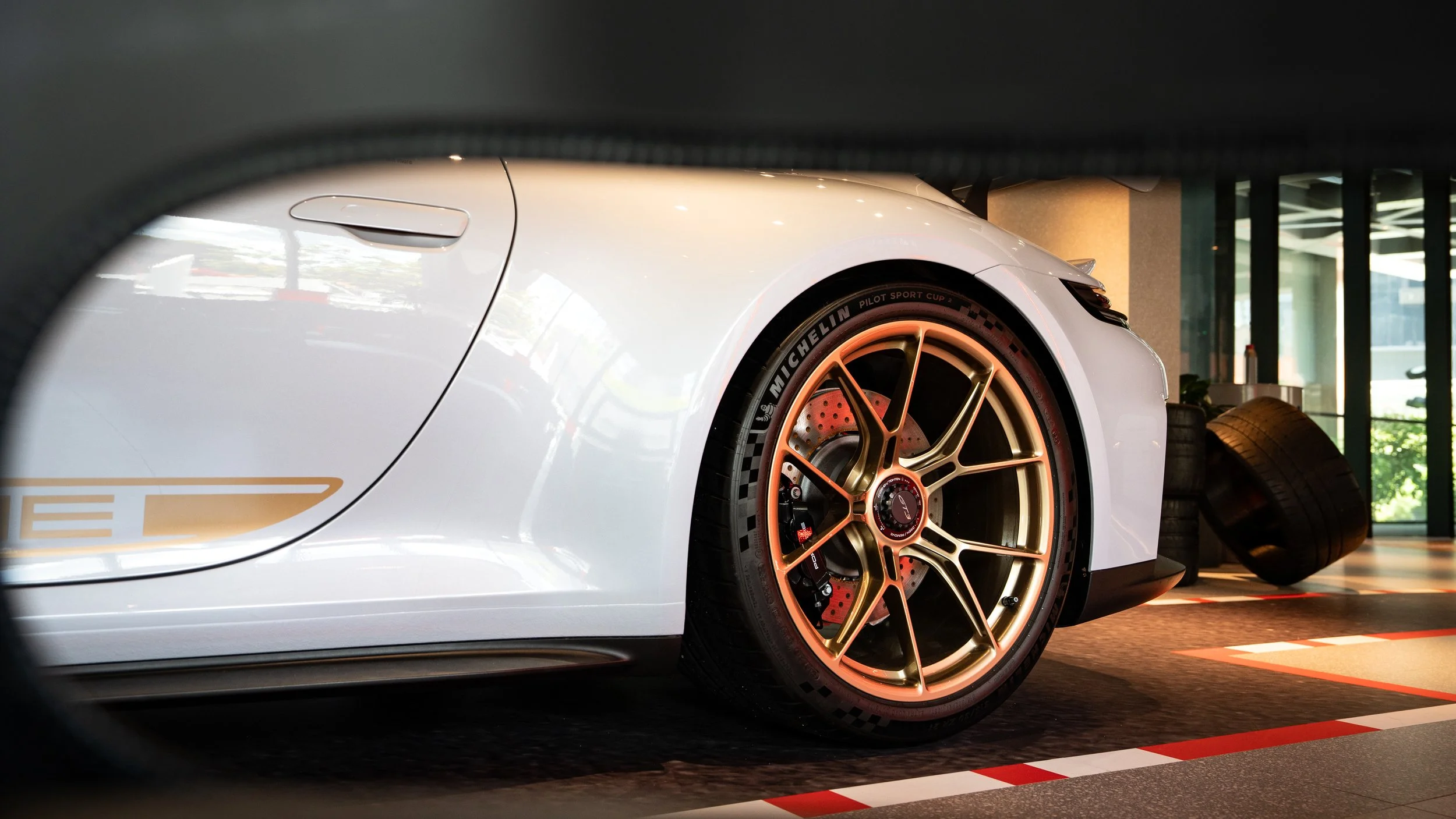 Close-up of a white sports car's front wheel and part of the car's body, with racing tires and a luxurious showroom background.