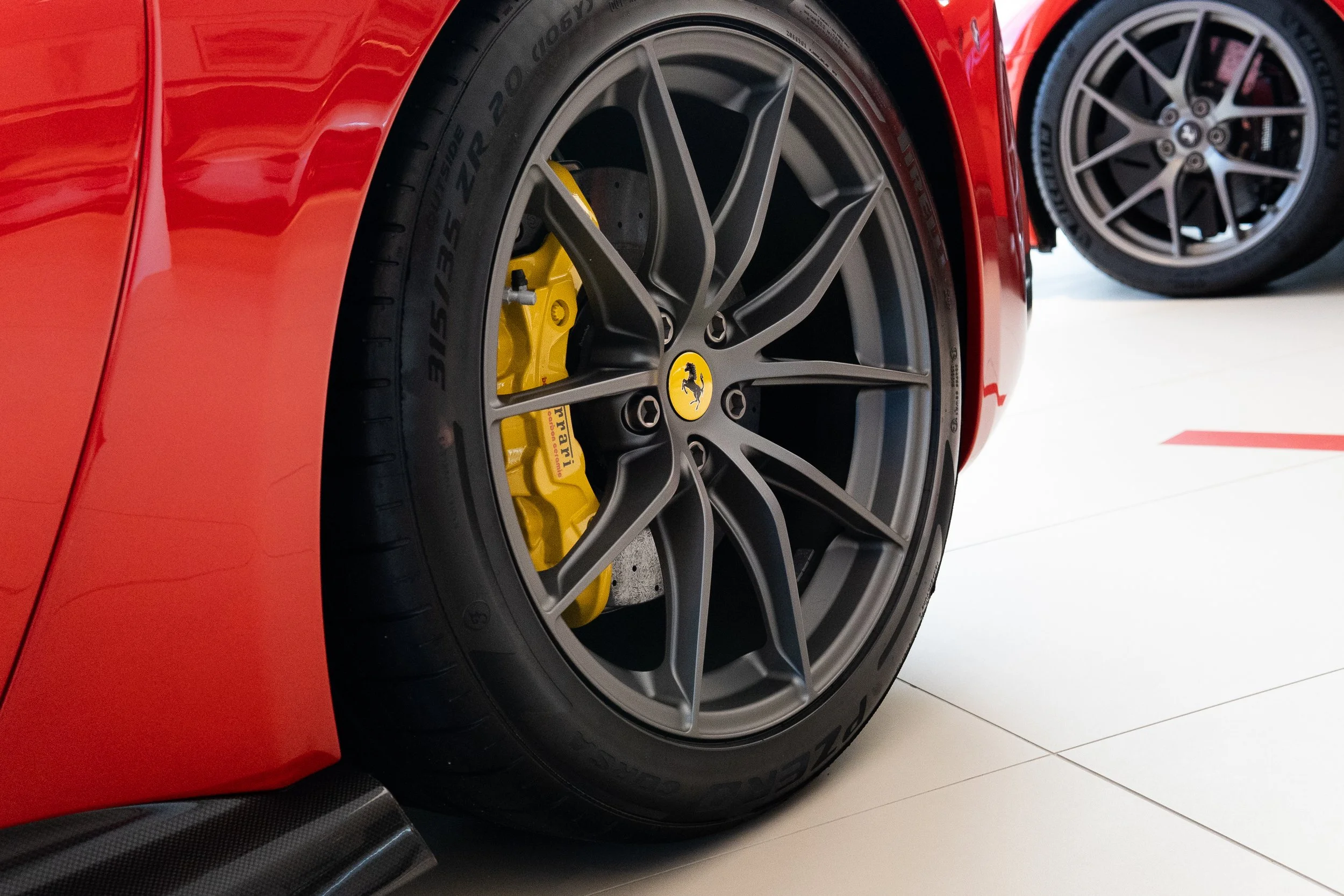 Close-up of a red Ferrari sports car wheel with a black run-flat tire, gray multi-spoke rim, and a yellow brake caliper with the Ferrari logo.