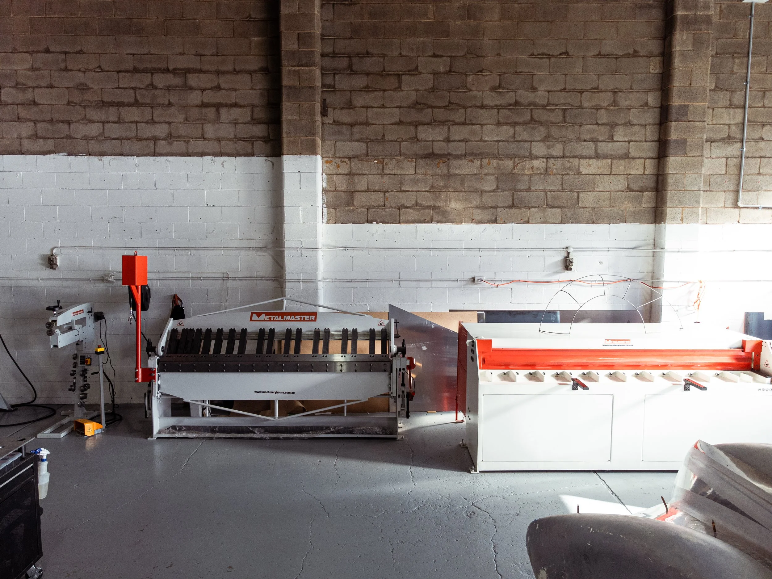 Industrial woodworking or metalworking machinery in a warehouse or workshop with exposed brick walls and concrete floor.