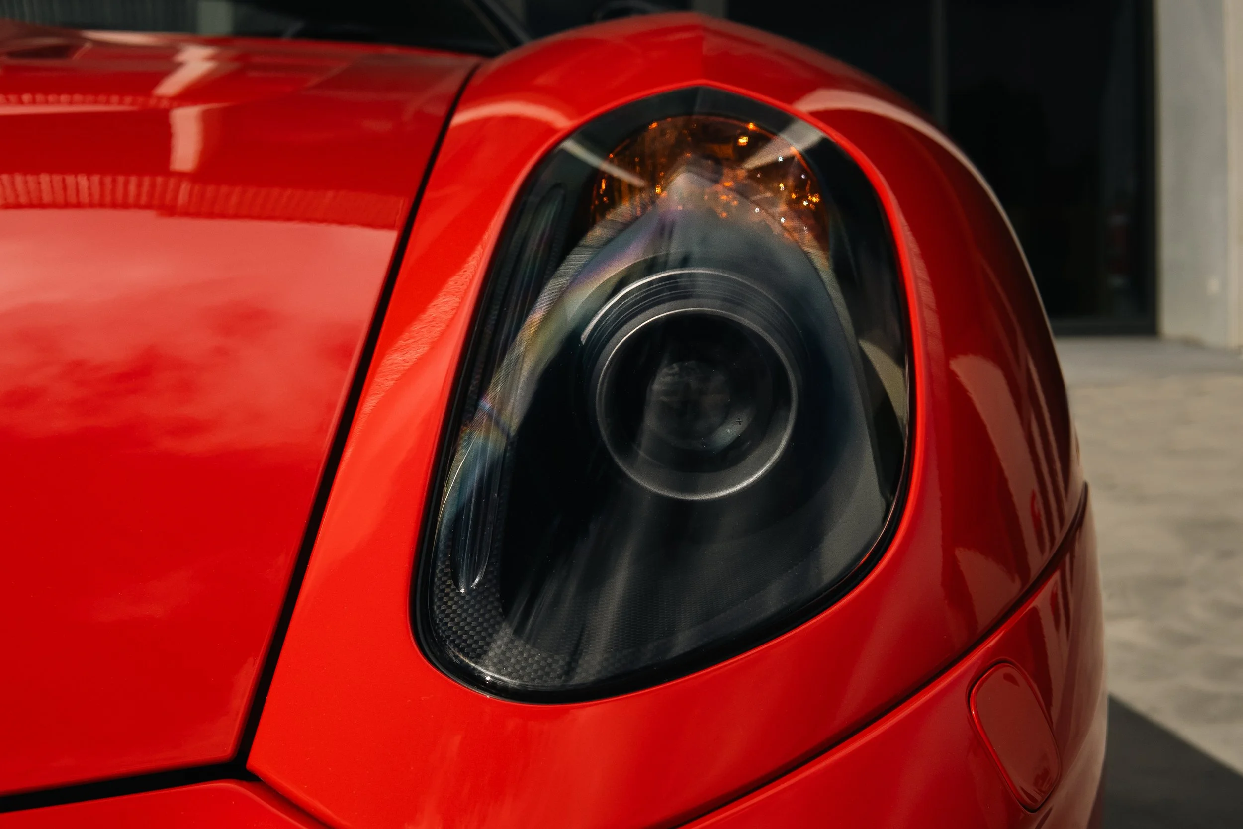 Close-up of the front left headlight of a red sports car, showing the glossy paint and sleek design.