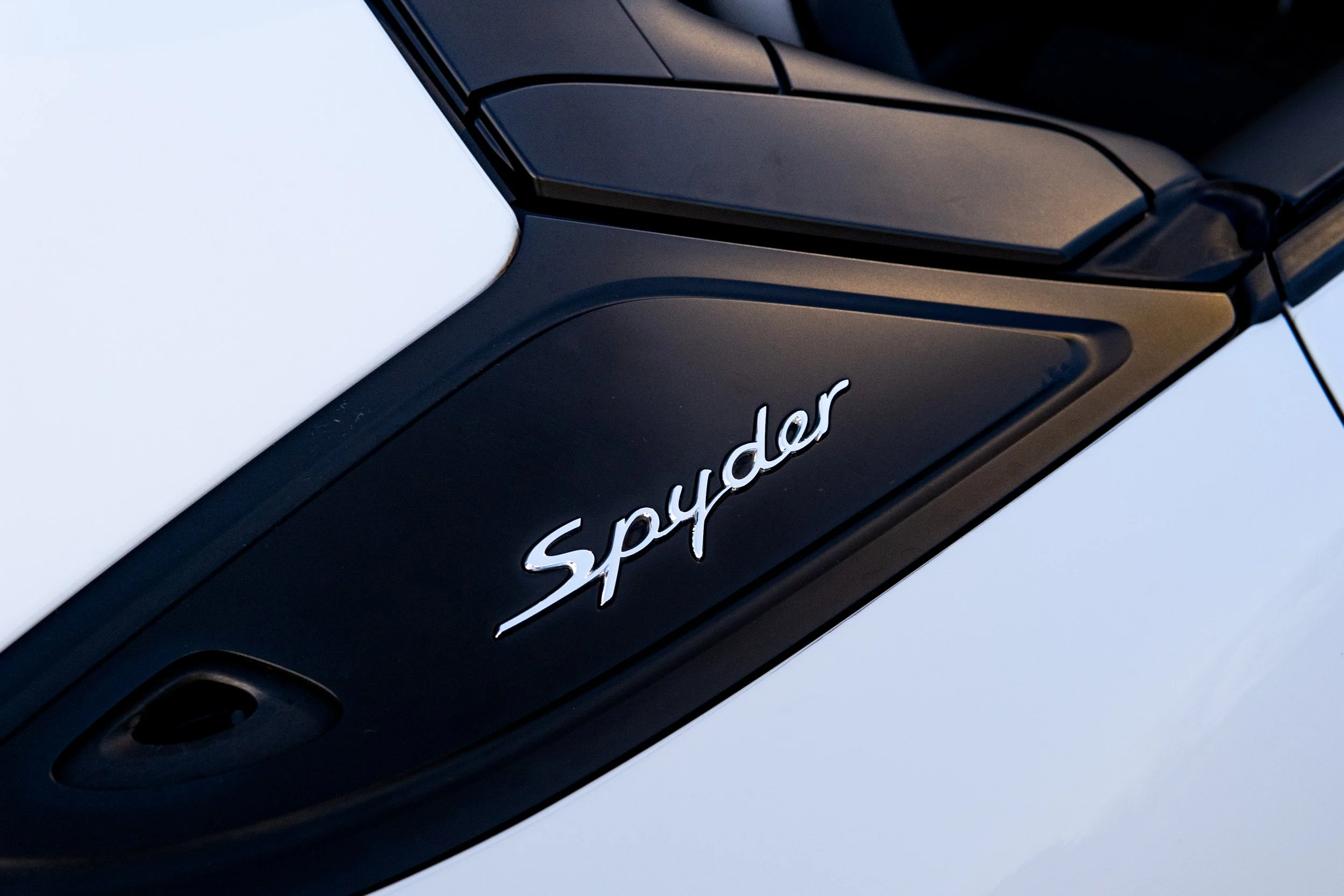 Close-up of a black part of a vehicle with the word 'Spyder' in silver cursive lettering.